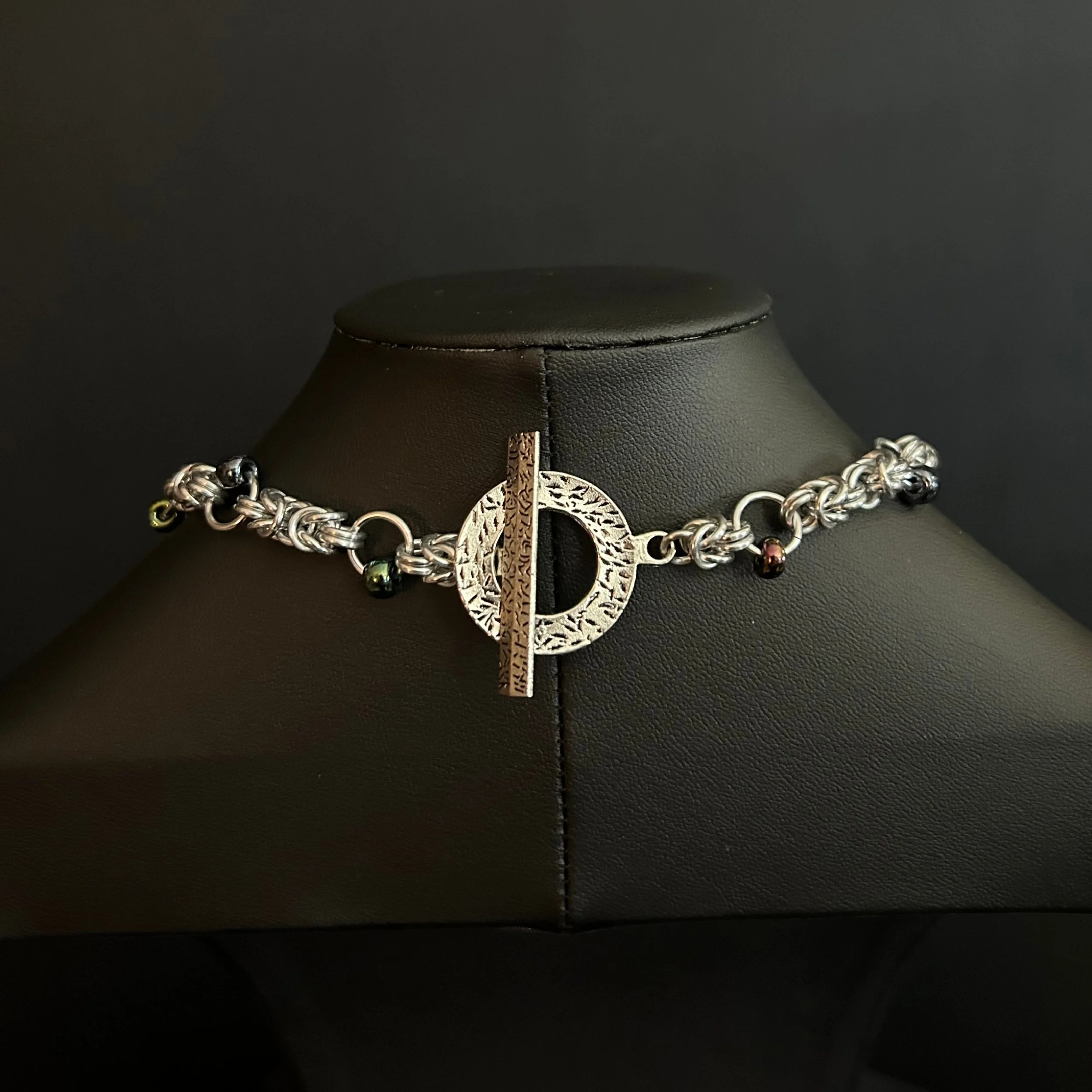 Midnight Tassel bracelet detail with silver chainmaille, dark beads, and a textured toggle clasp on a black display