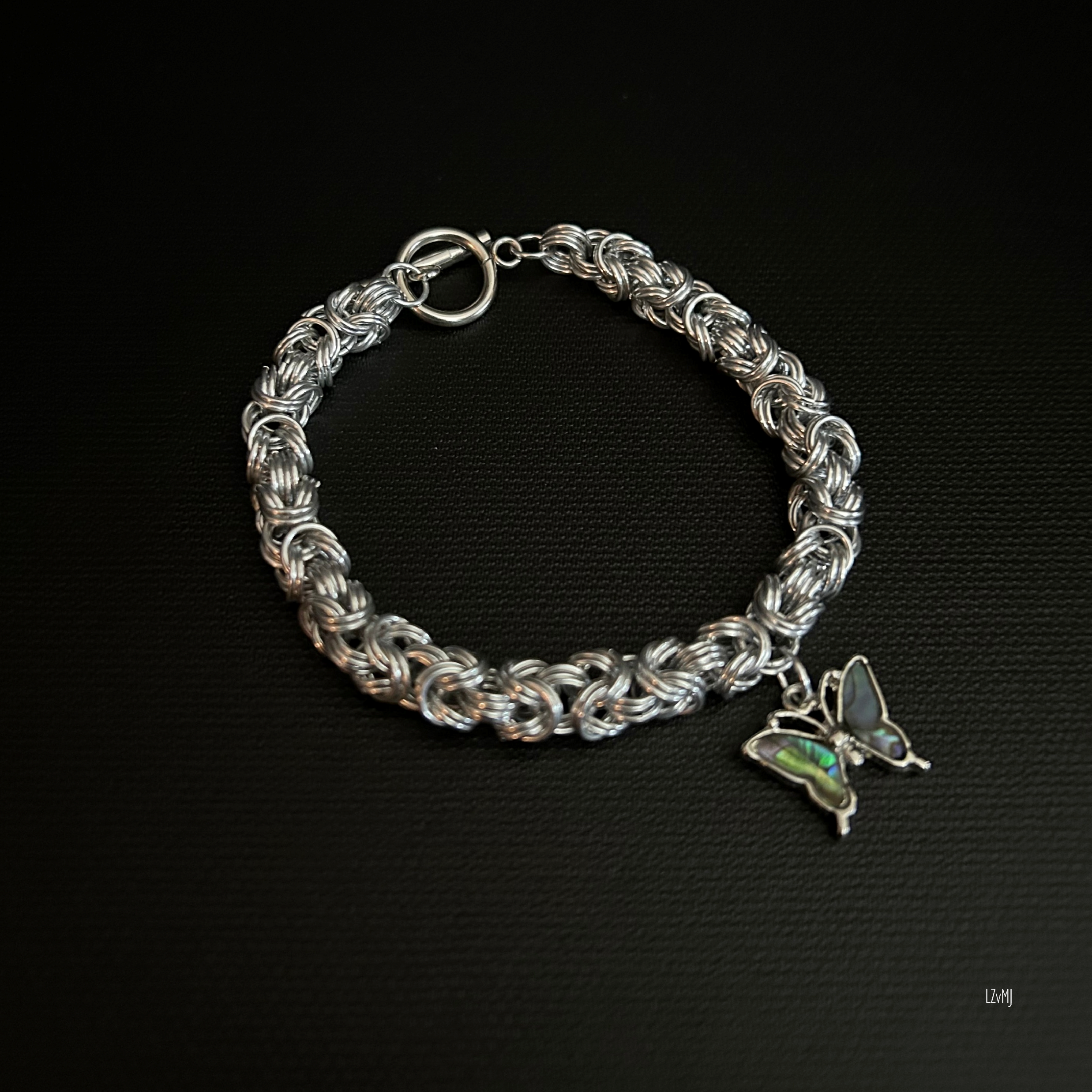 “Highland Wing bracelet laid flat in a round shape showing the double‑weave Byzantine rings and butterfly charms.”