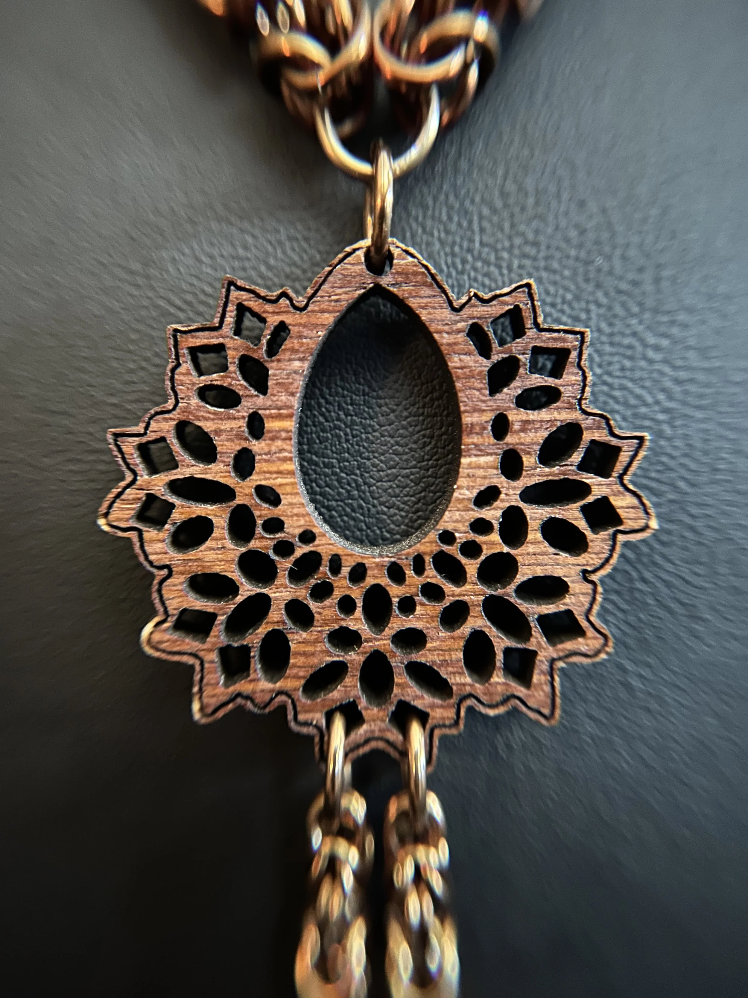 Close‑up of the pendant’s lower section showing two short bronze chain tassels, each ending in a small amber bead.