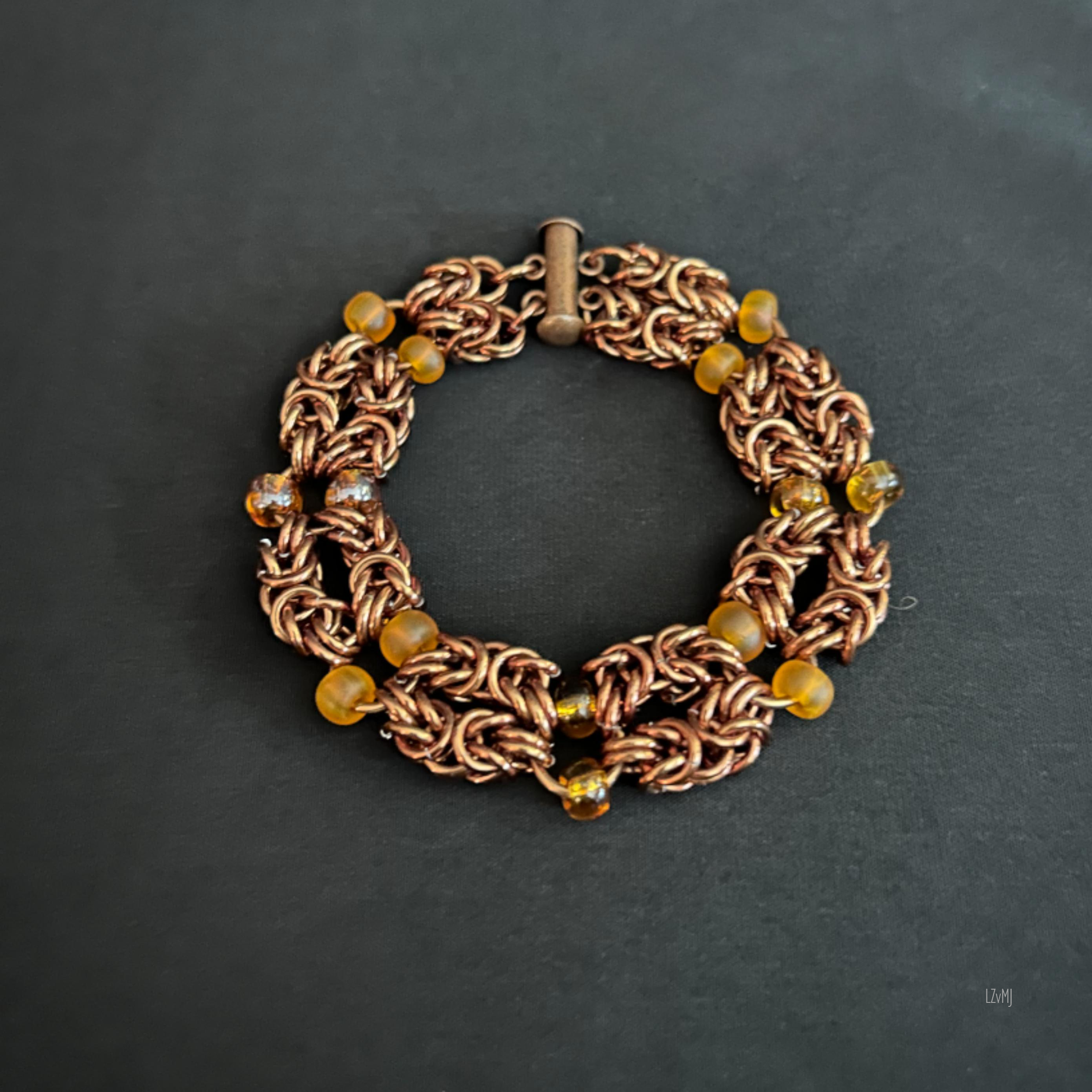 “Bronze Amberlight bracelet laid flat in a round shape showing bronze rings and amber beads.”