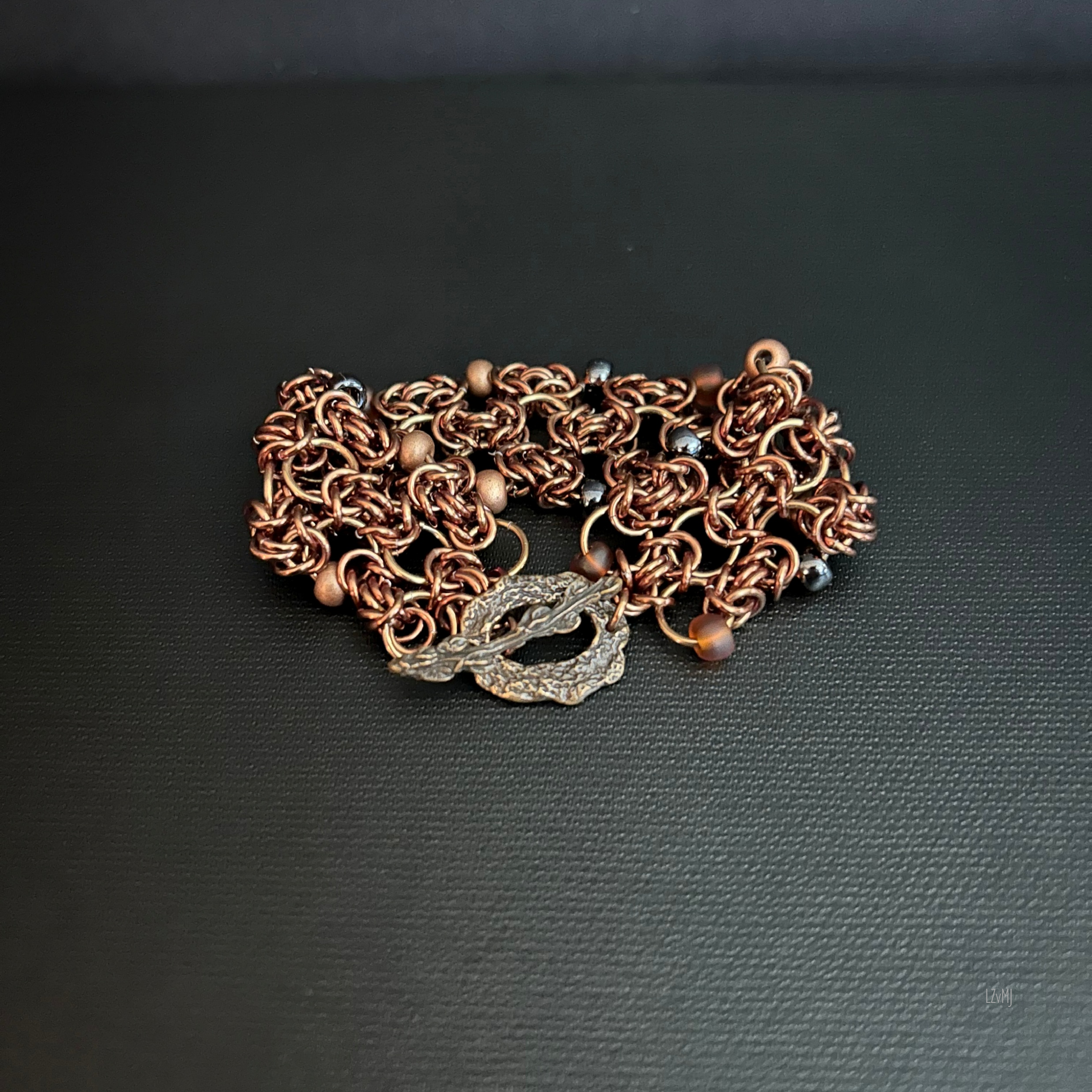 “Bronze Ember bracelet laid flat with the clasp closed, showing the Byzantine weave and beads.”