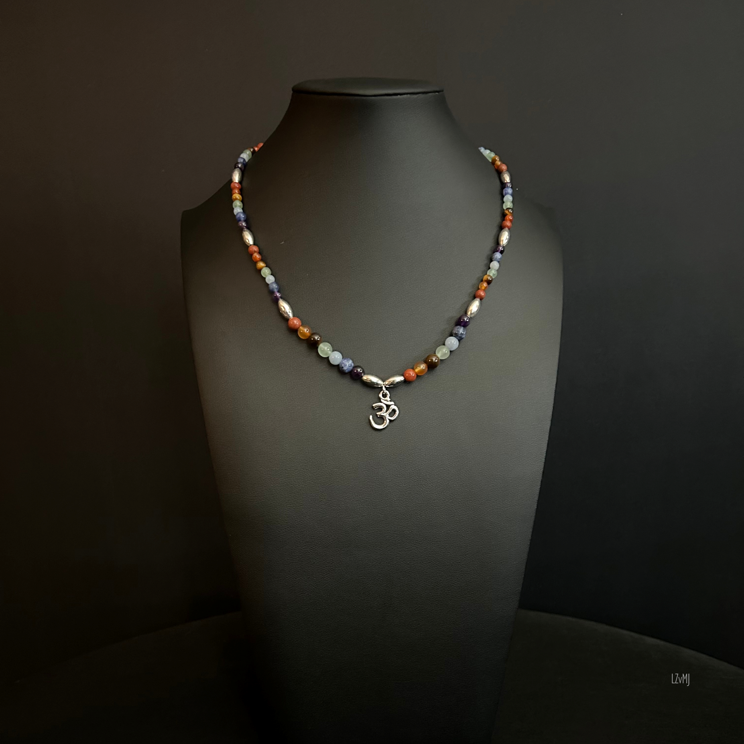Om Balance necklace displayed on a black bust, with multicolor gemstone beads and a silver Om pendant at the center