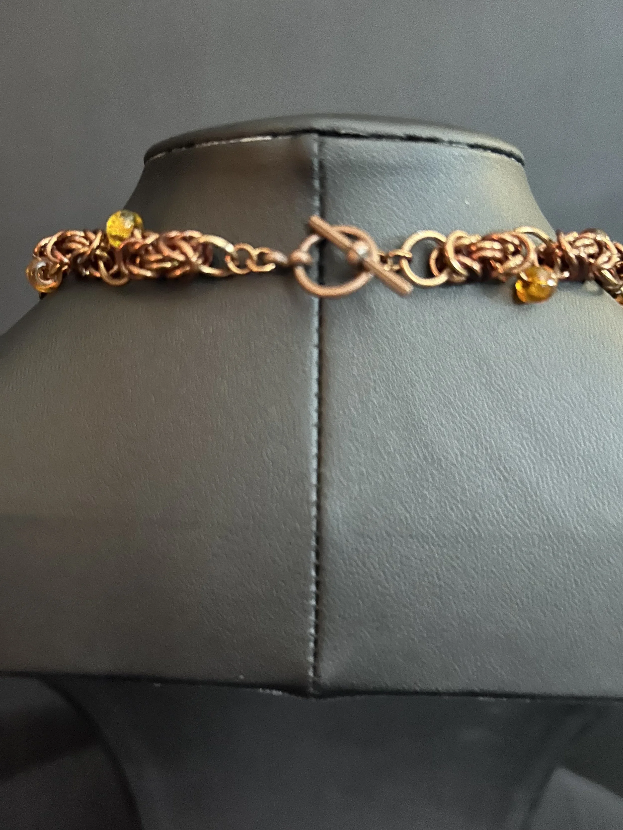 Toggle clasp in bronze tones shown in close‑up, with the circular ring and straight bar visible along with nearby amber beads.