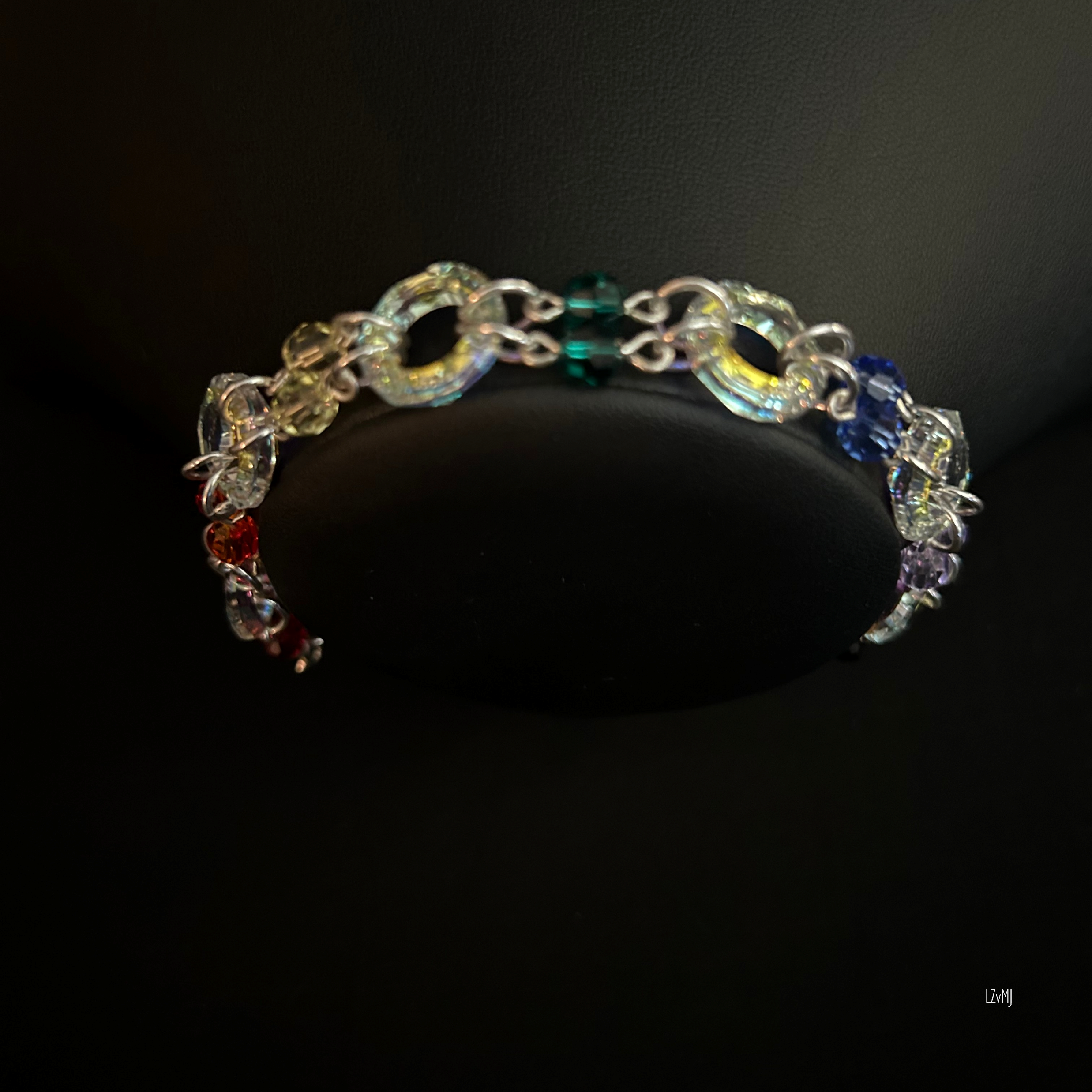 Close-up of the chainmaille rosette structure, showing the interwoven sterling rings and the faceted Swarovski crystals. The iridescent finish on the rings reflects subtle blues and purple