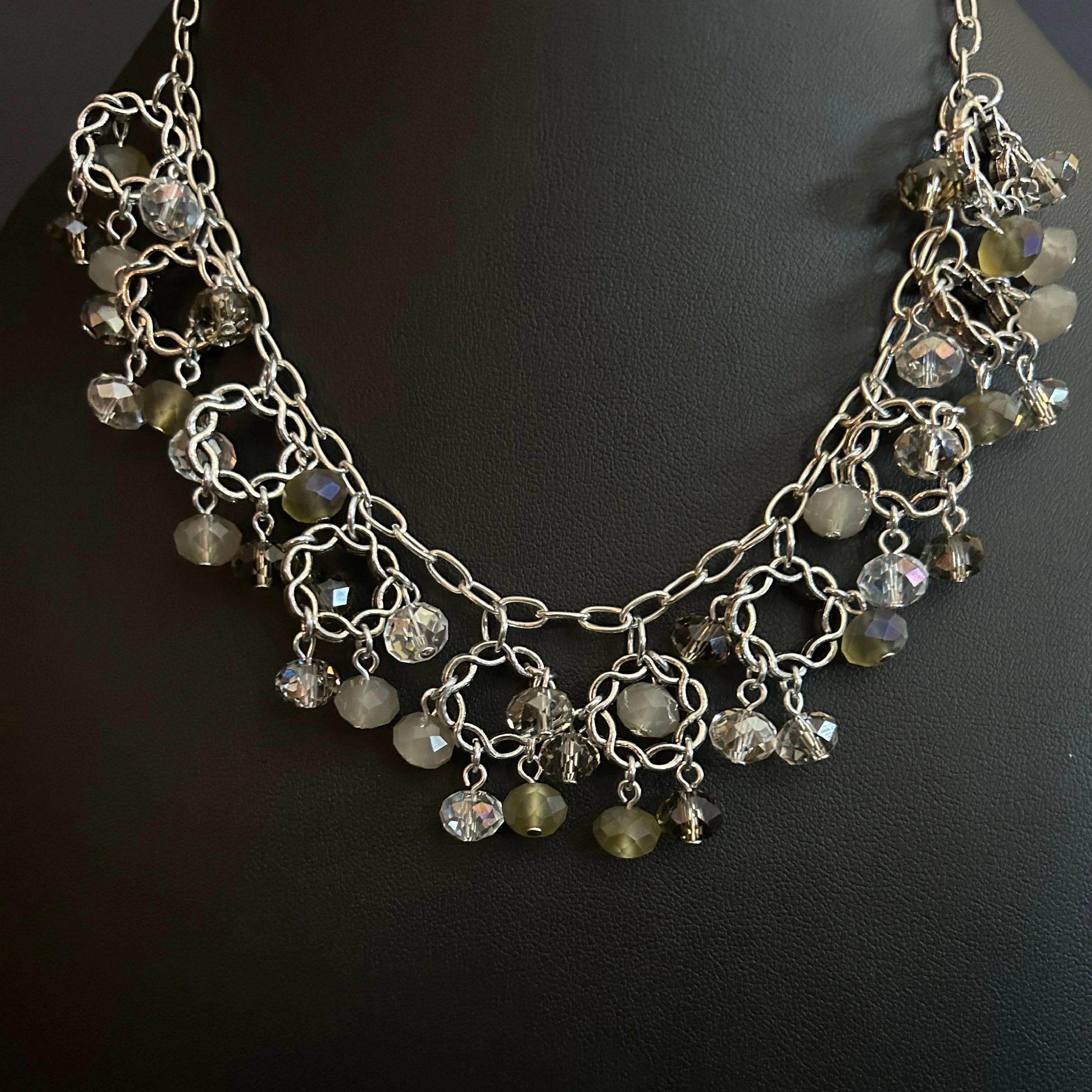 Close-up of the Crystal Orbit necklace showing the interlinked silver rings and central clasp framed by black beads