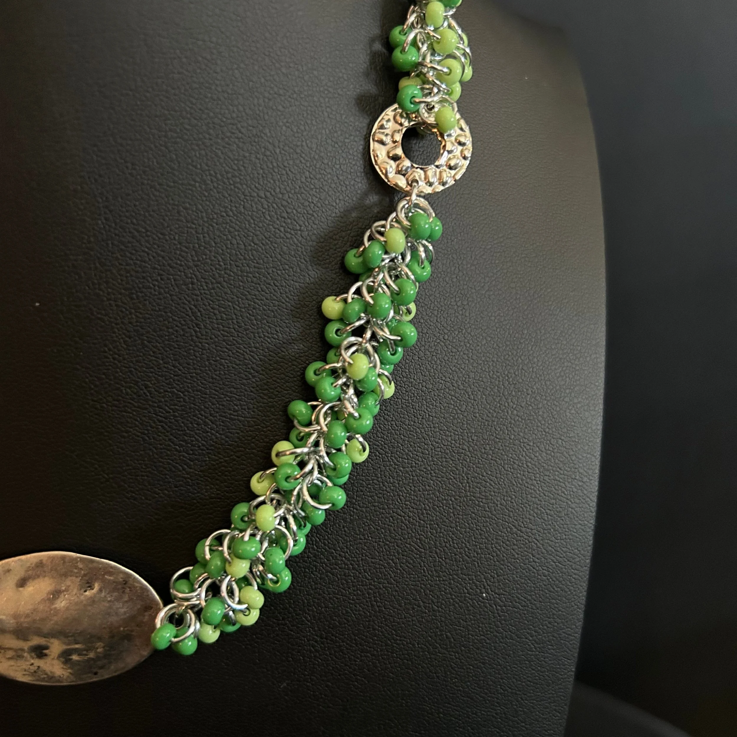 “Detail of the shaggy‑loop weave with light‑green and pea‑green beads and silver rings.”