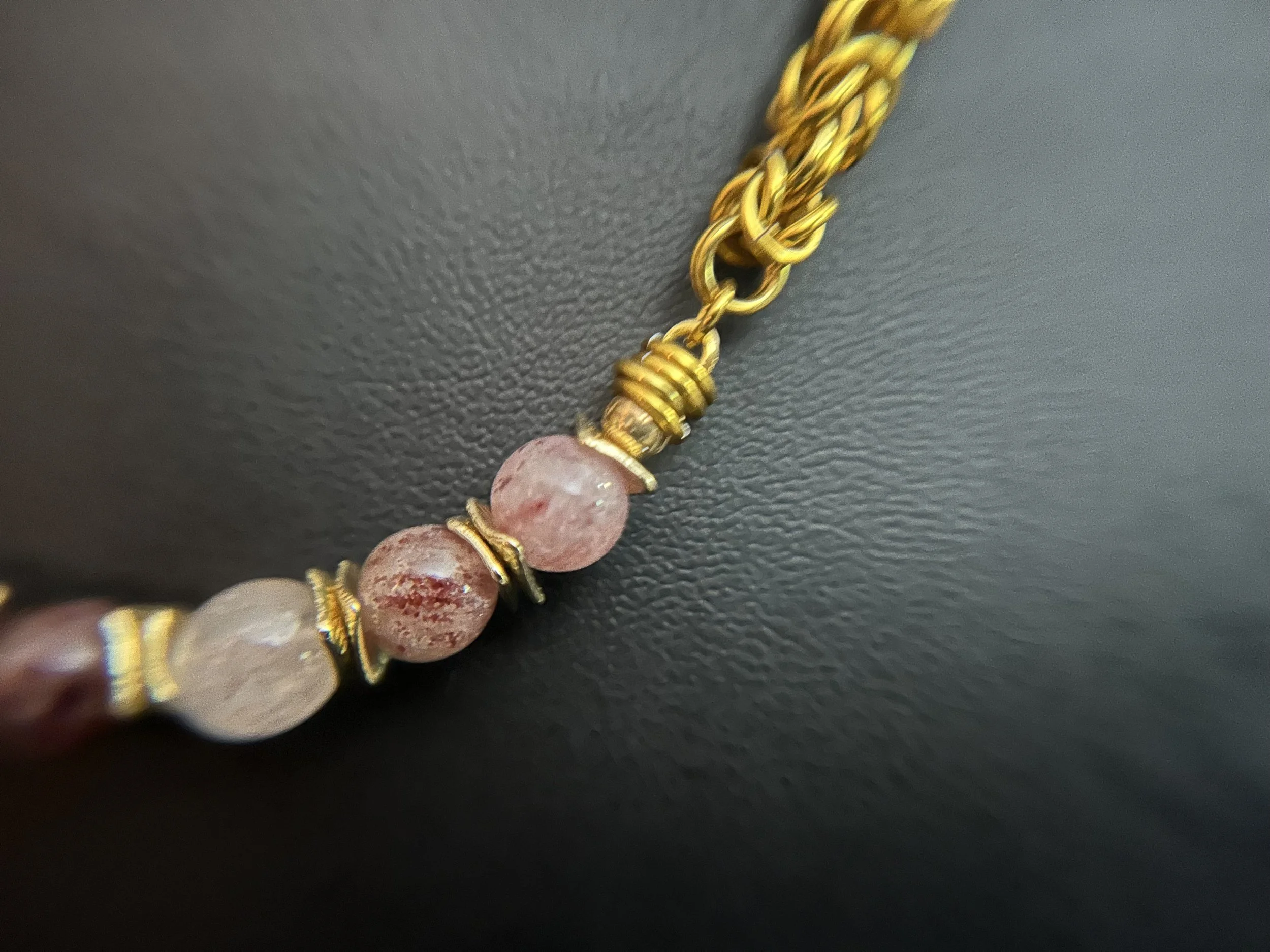 Detail of hand‑woven gold‑tone chainmaille necklace with seven 8mm strawberry quartz beads and gold‑plated spacers,