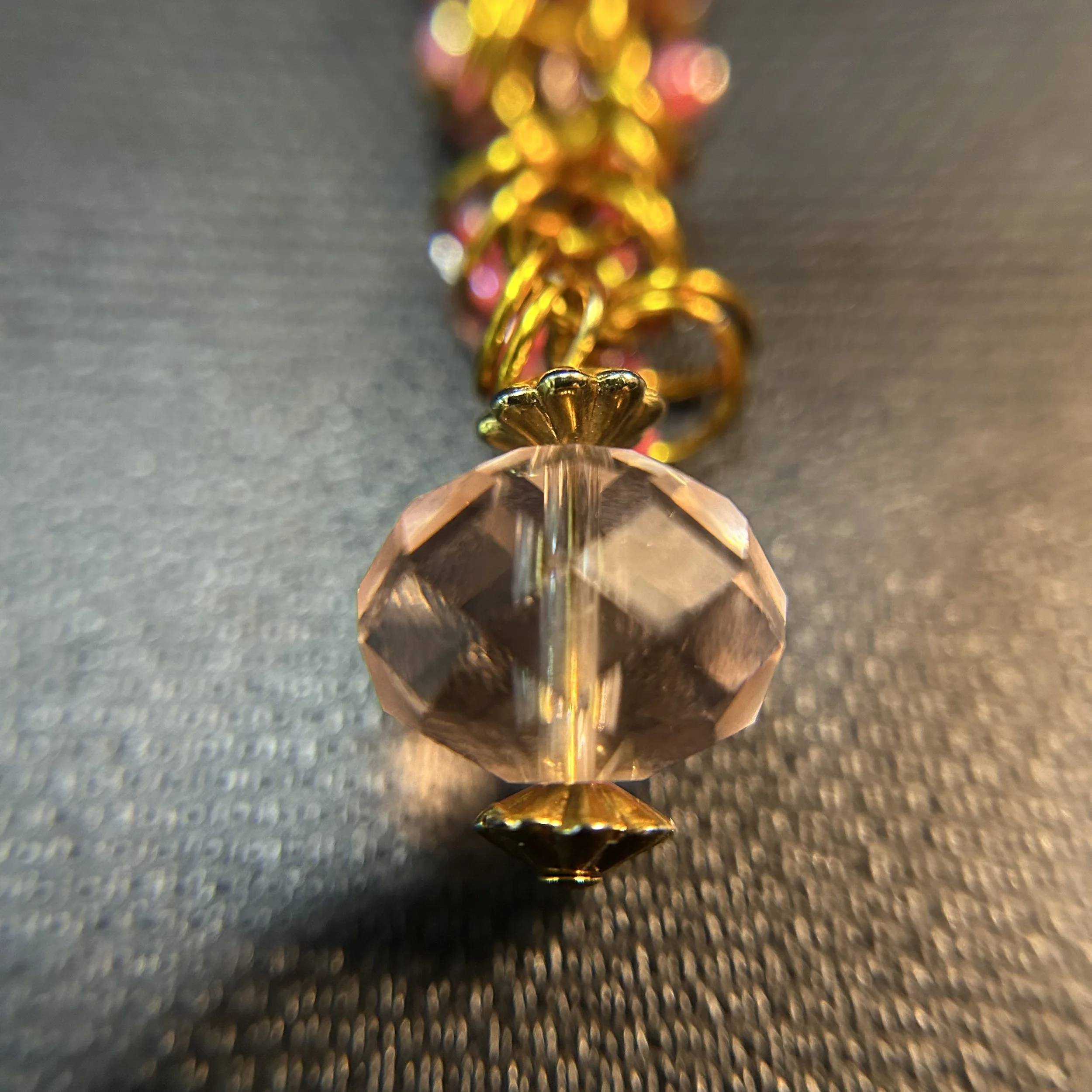 “Close-up of faceted crystal focal with gold caps and pink bead accents on gold purse charm.”