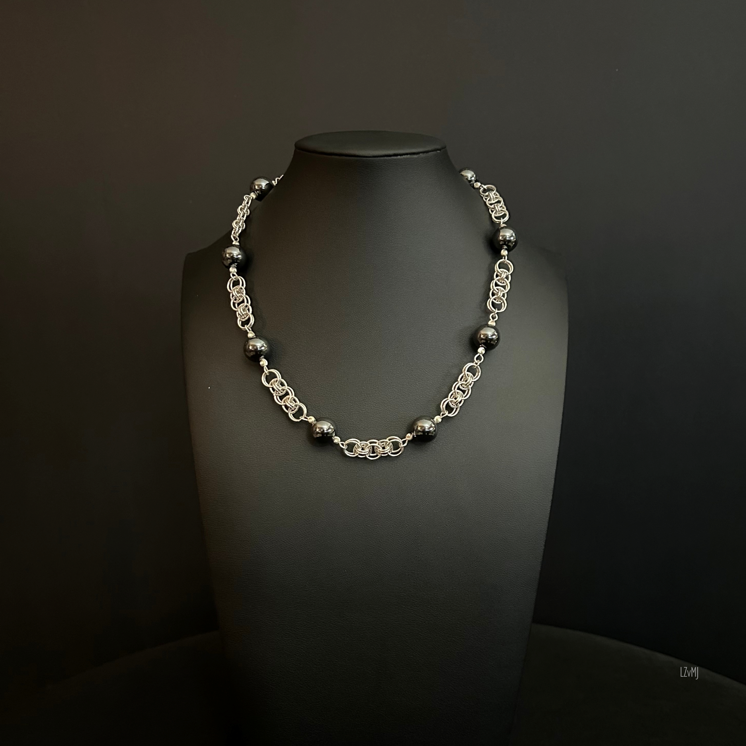 Silver Orbit necklace displayed on a black bust, featuring a sterling silver helm weave with large polished hematite beads