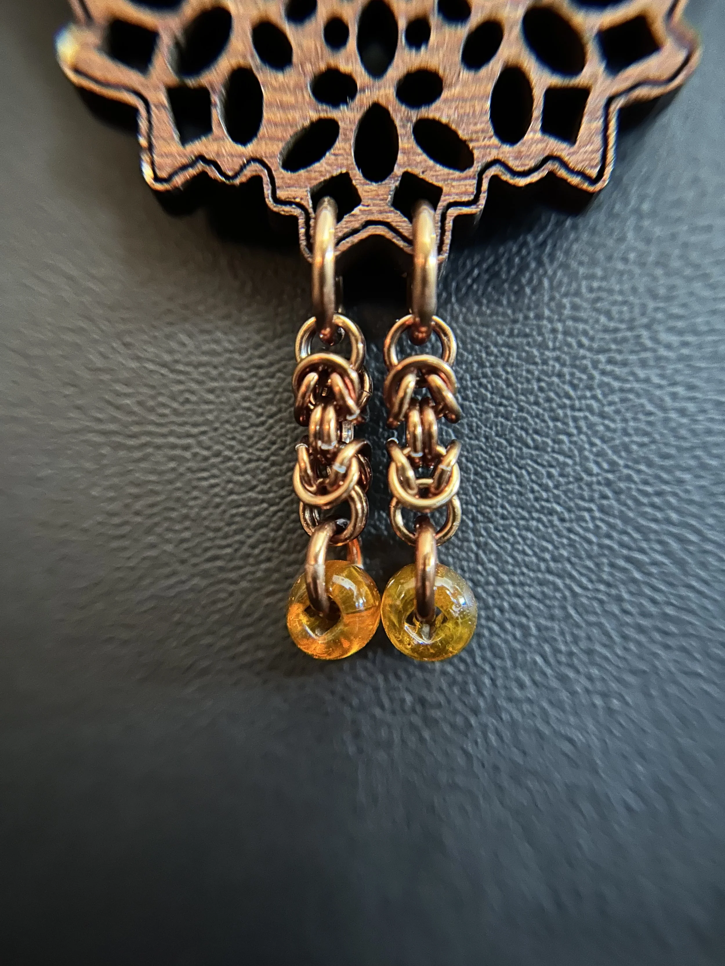 Close‑up of the pendant’s lower section showing two short bronze chain tassels, each ending in a small amber bead.