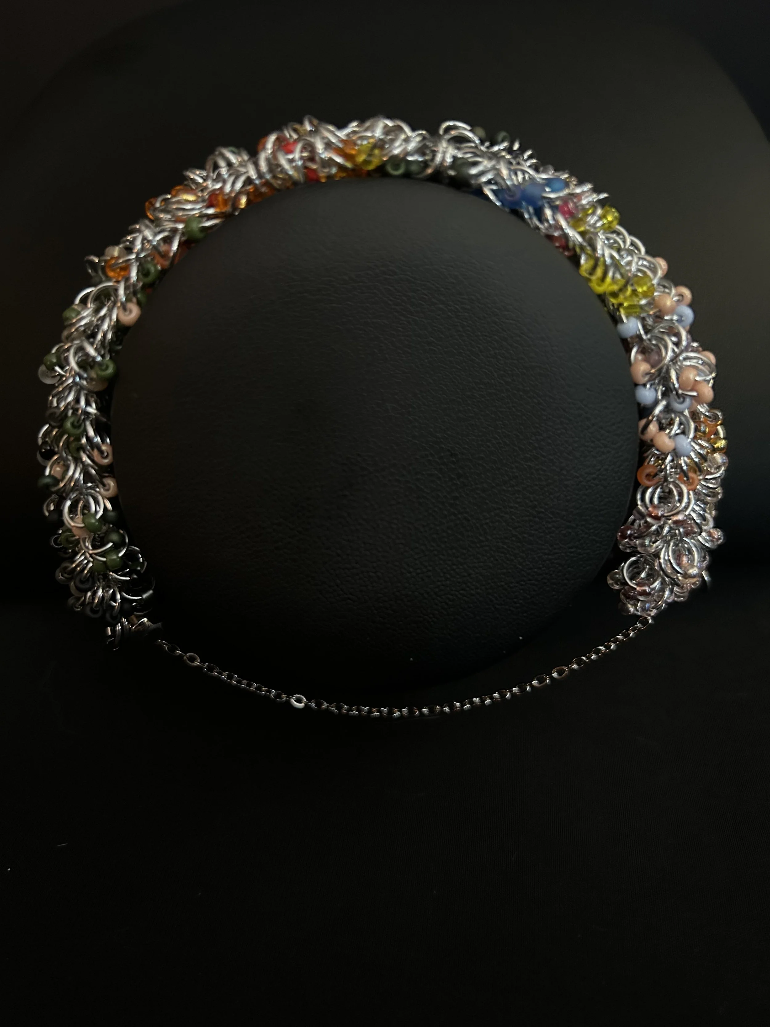 Blue Ridge Autumn bracelet draped on a black jewelry bust, featuring silver aluminum chainmaille and colorful 8/0 Miyuki beads inspired by Blue Ridge fall tones.