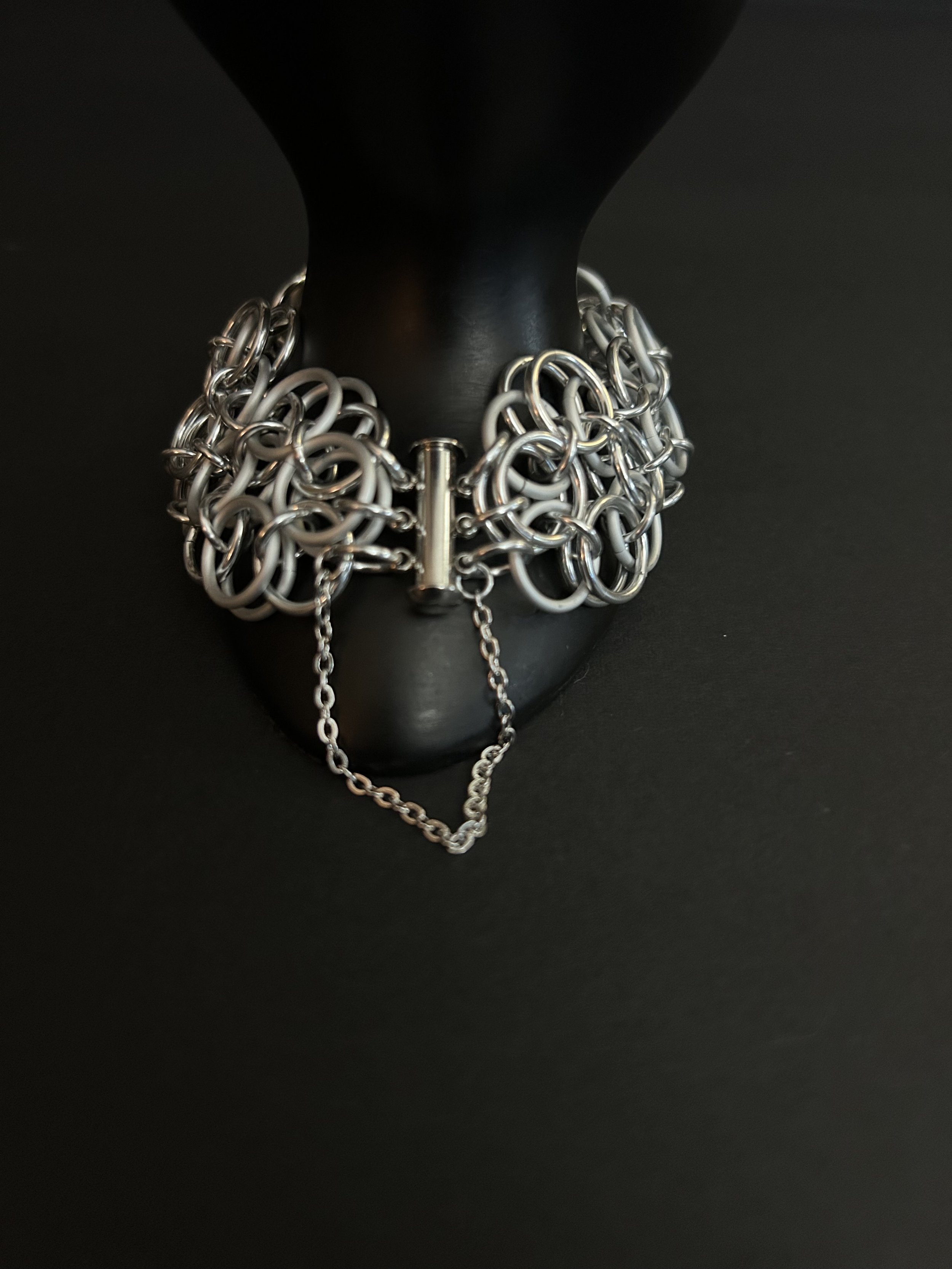 The clasp of a chainmaille bracelet woven in a helm rosette pattern on a black hand prop