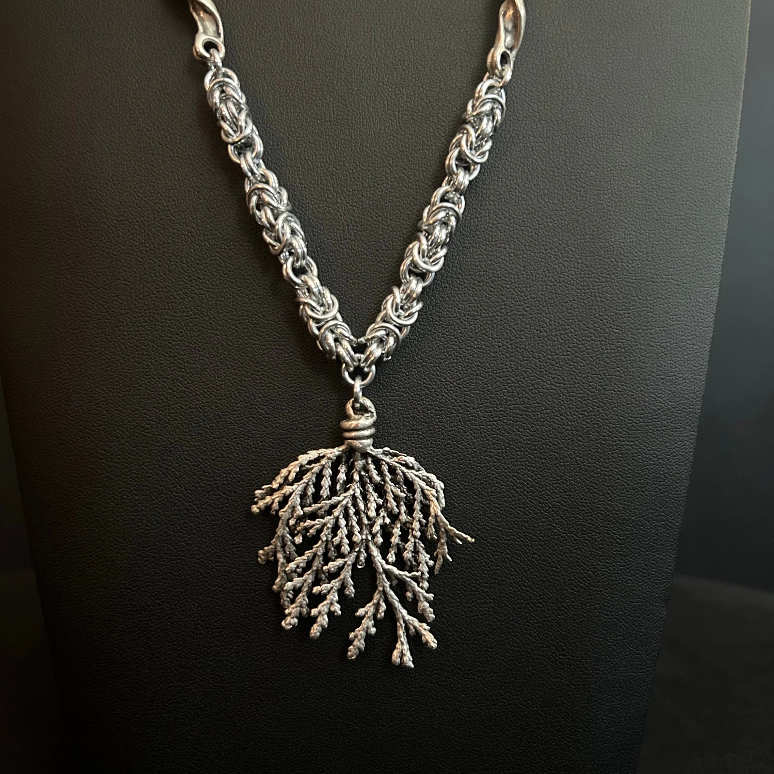 Silver Forest necklace with a thick woven chain and a large textured branching pendant, shown against a black background