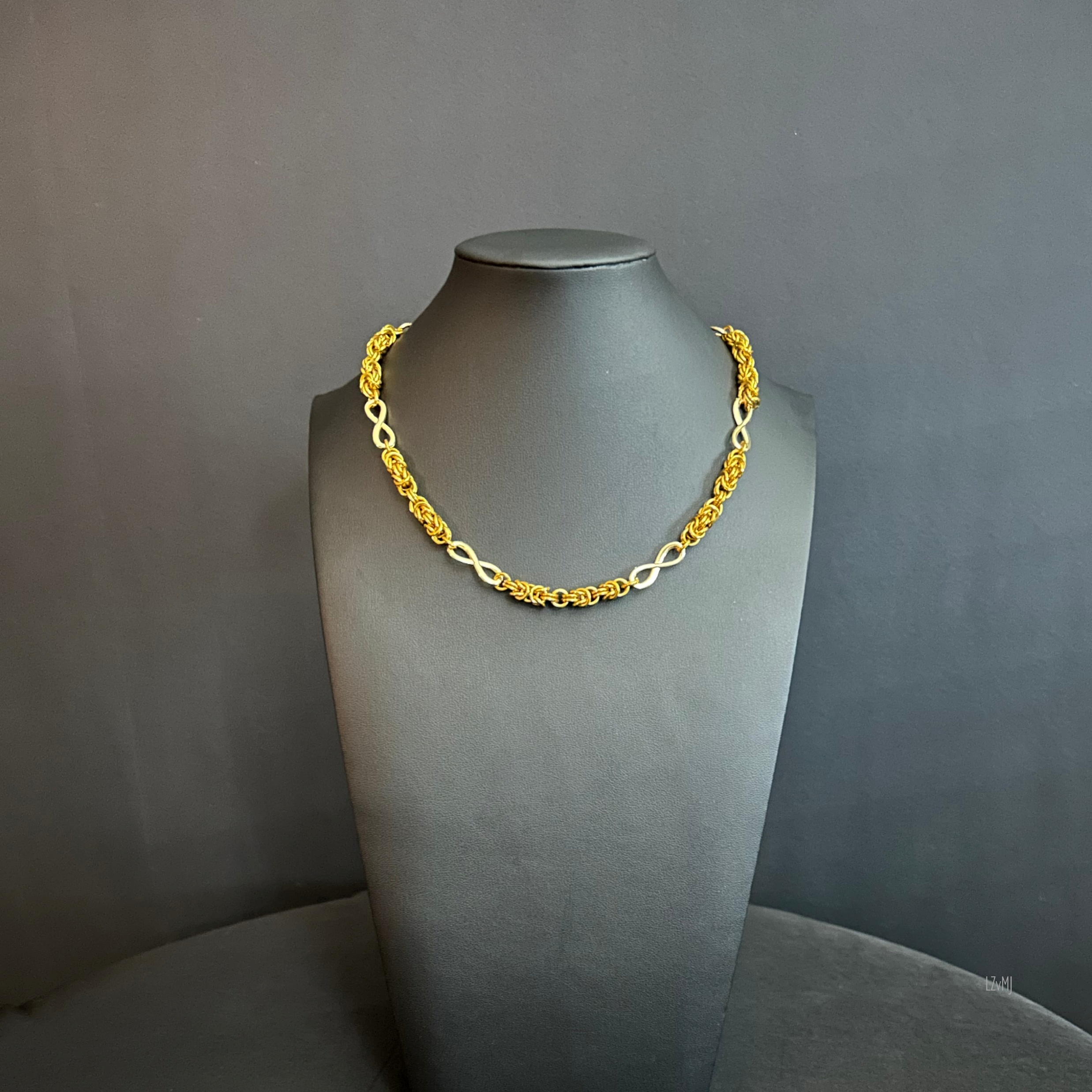 Golden Infinity necklace displayed on a black bust, featuring alternating Byzantine chainmaille segments and gold infinity connectors