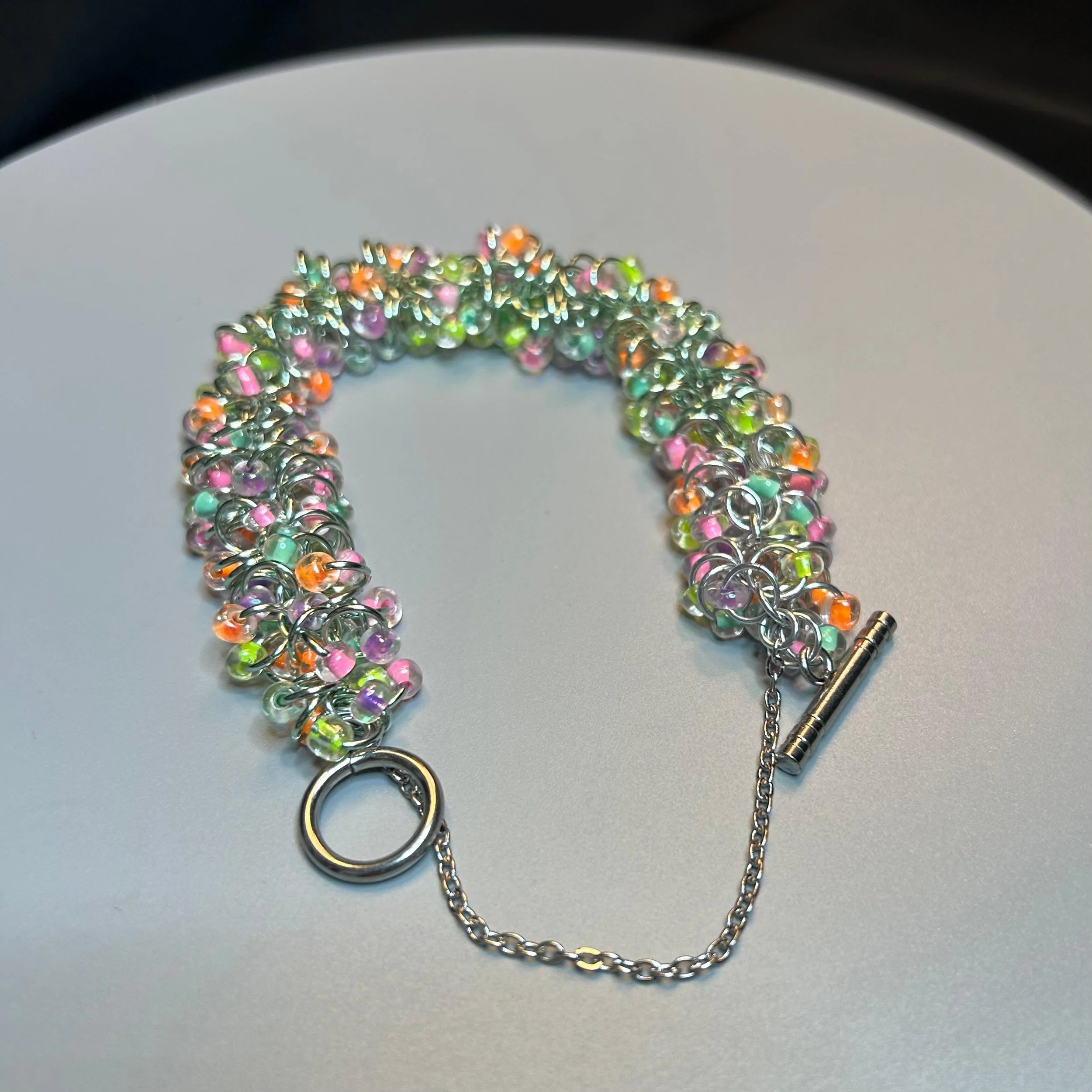Bracelet laid flat with toggle clasp open, showing ring structure and pastel bead placement.