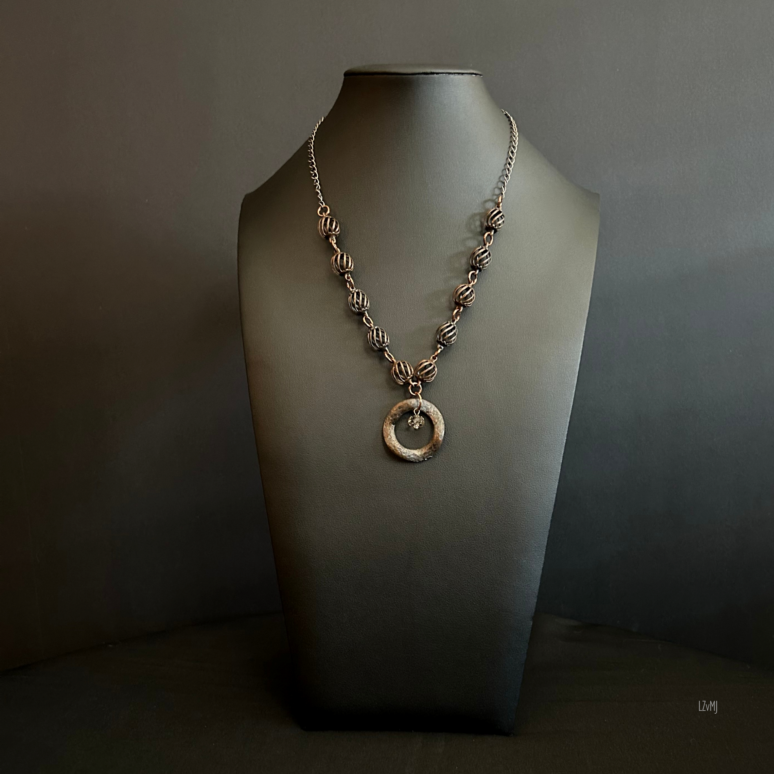 “Full view of the bronze bead necklace with textured focal and crystal center.”