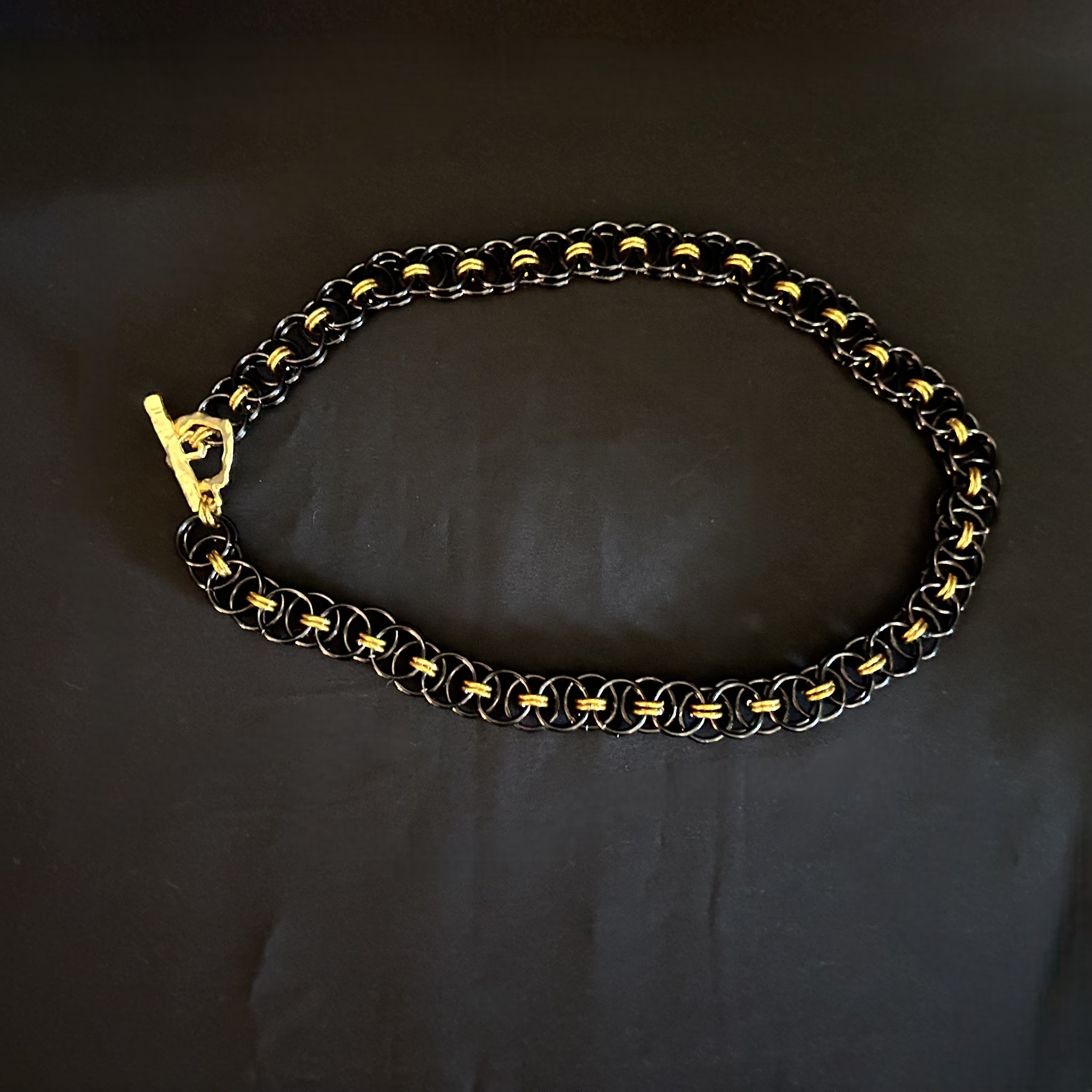 Blackgold Ladder necklace laid flat to show the repeating black and gold aluminum pattern and clean geometric weave.