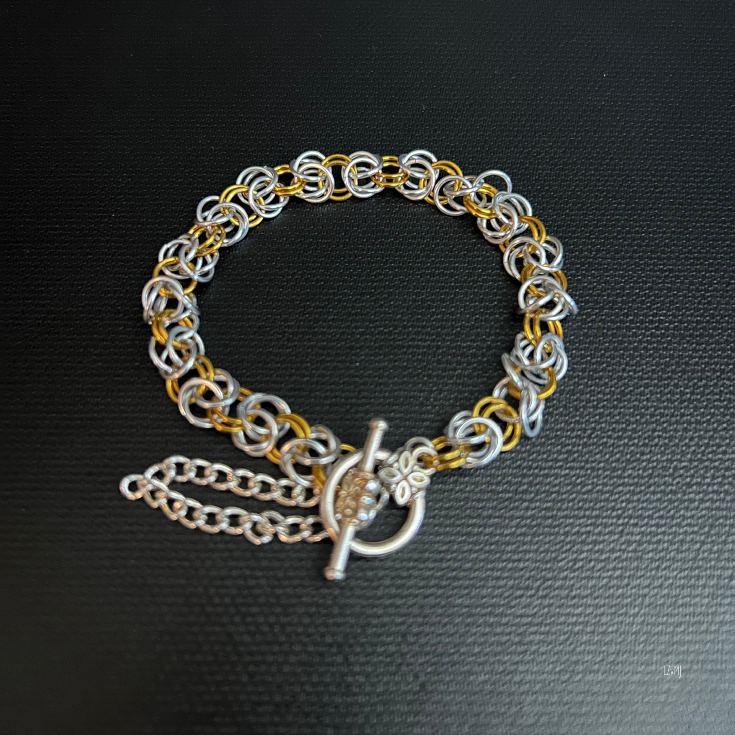 “Silvergold Byzantine bracelet laid in a square‑round shape with the silver toggle clasp visible.”