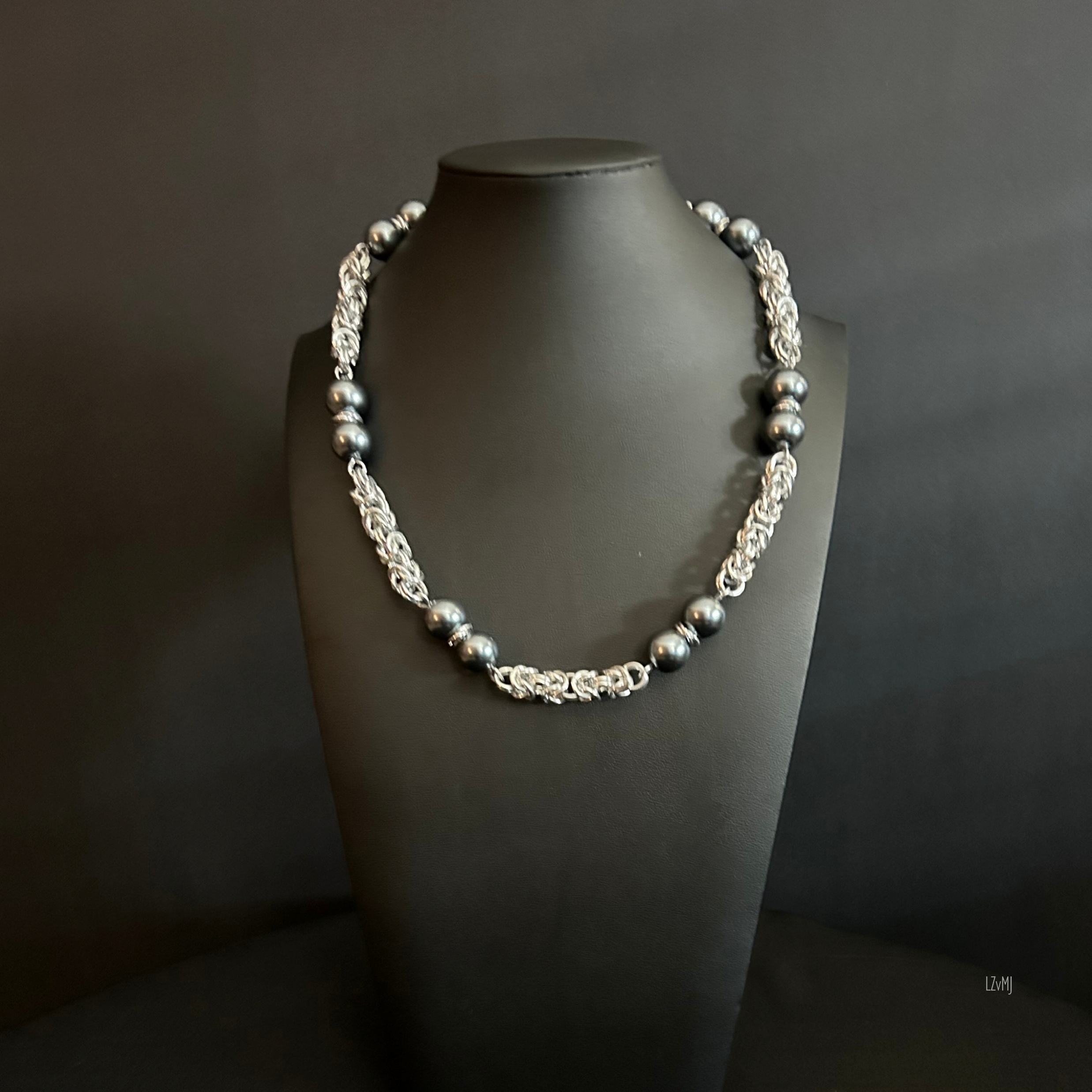 “Necklace shown fully extended, highlighting the aluminum weave and gunmetal pearls.”