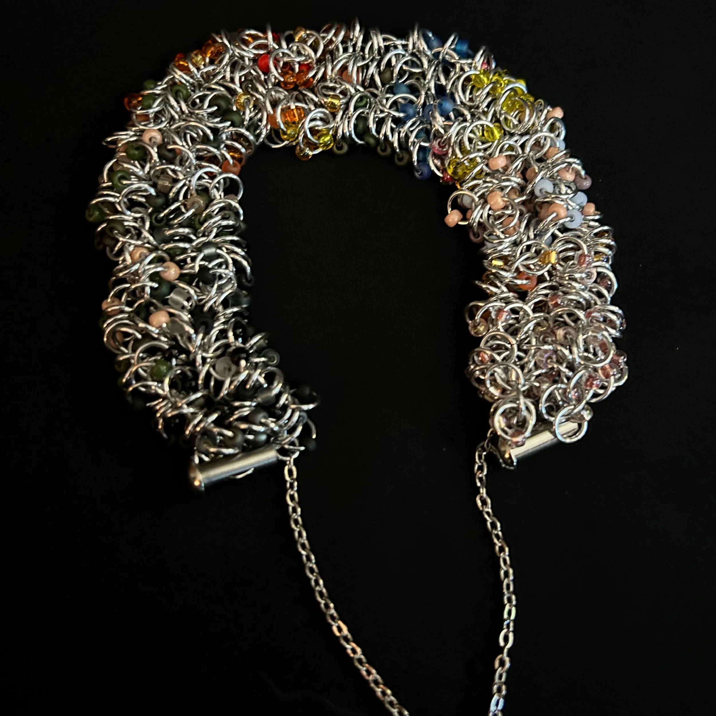 “Bracelet laid flat with the clasp open, showing rings and autumn‑tone beads.”