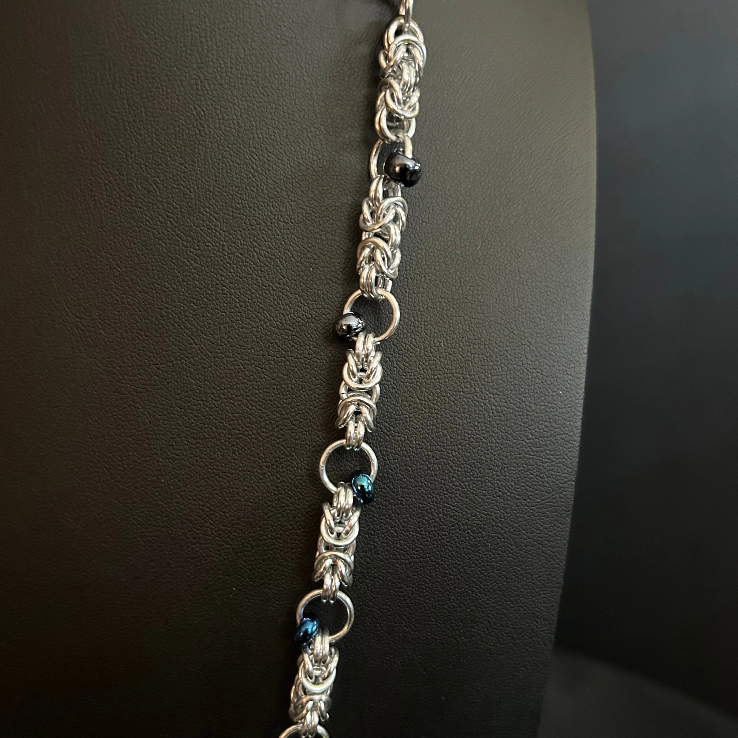 Close-up of the Midnight Tassel necklace showing the silver chainmaille weave and small dark iridescent beads spaced along the chain