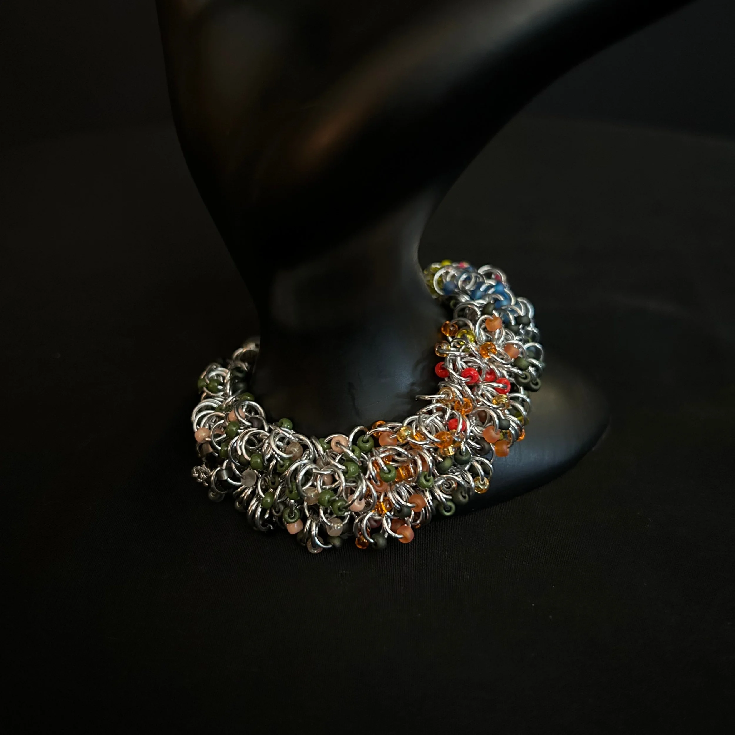 “Bronze and silver bracelet with autumn‑tone beads draped over a display prop.”