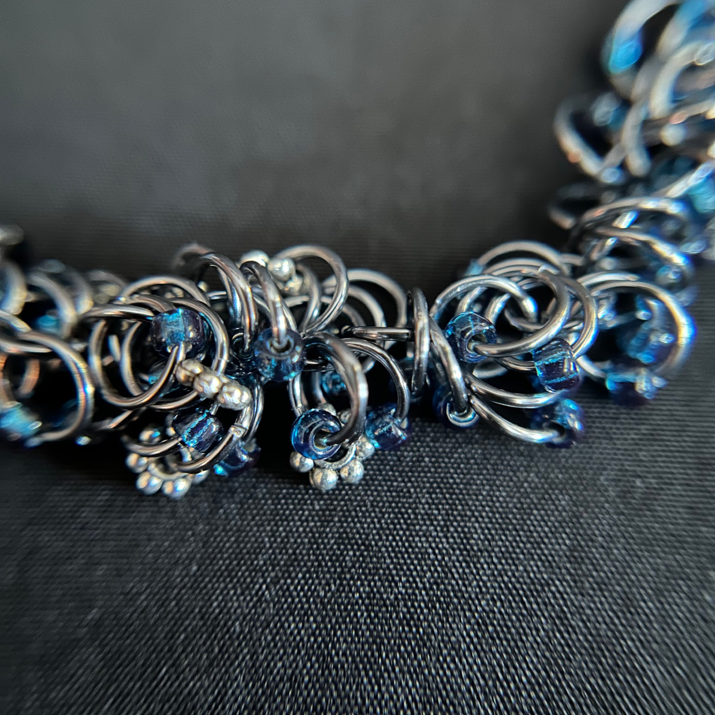 “Detail of the Black Ice shaggy‑loop rings with dark blue translucent beads.”