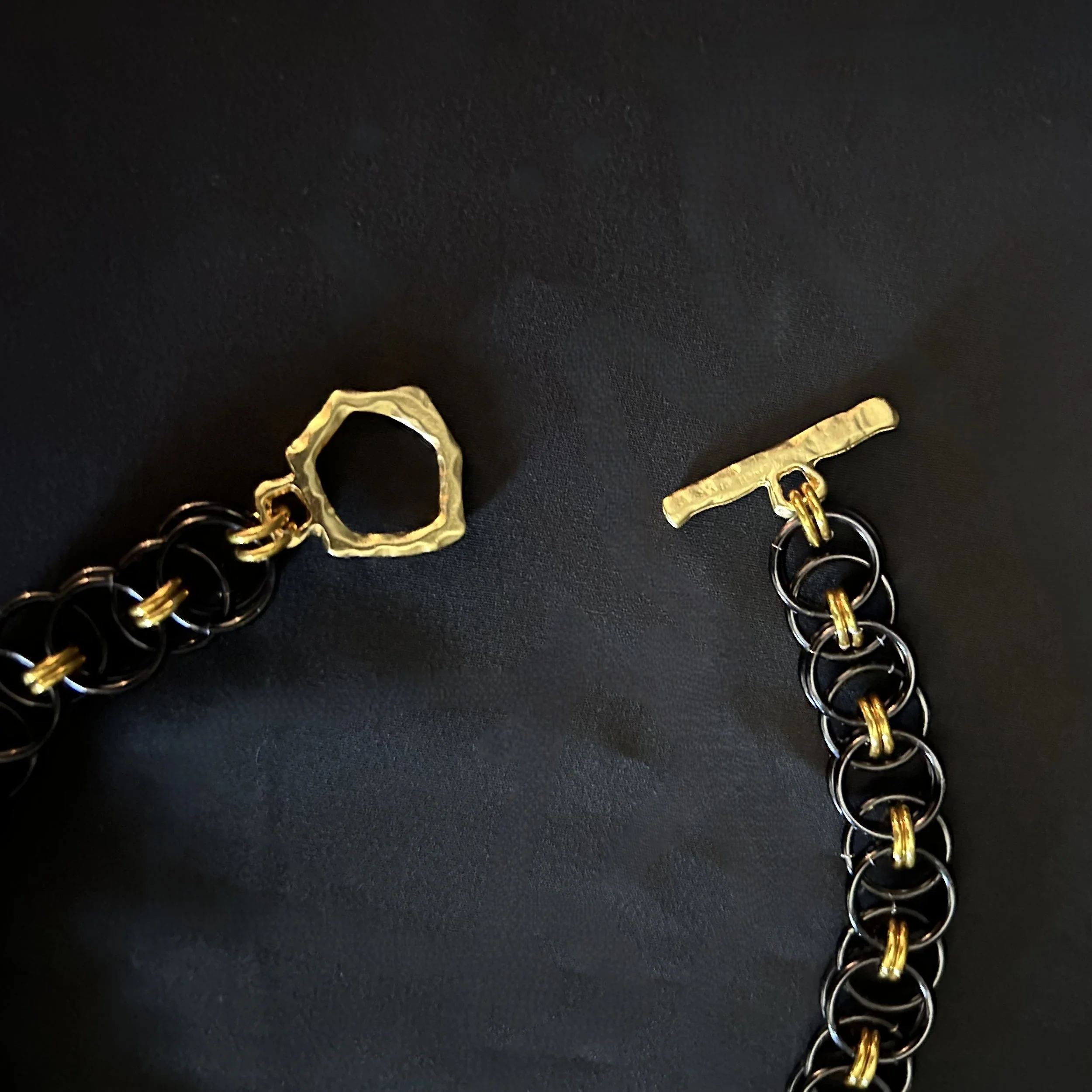 Close-up of the Blackgold Ladder necklace toggle clasp laid flat, showing the sculptural black and gold aluminum rings and clean connection.
