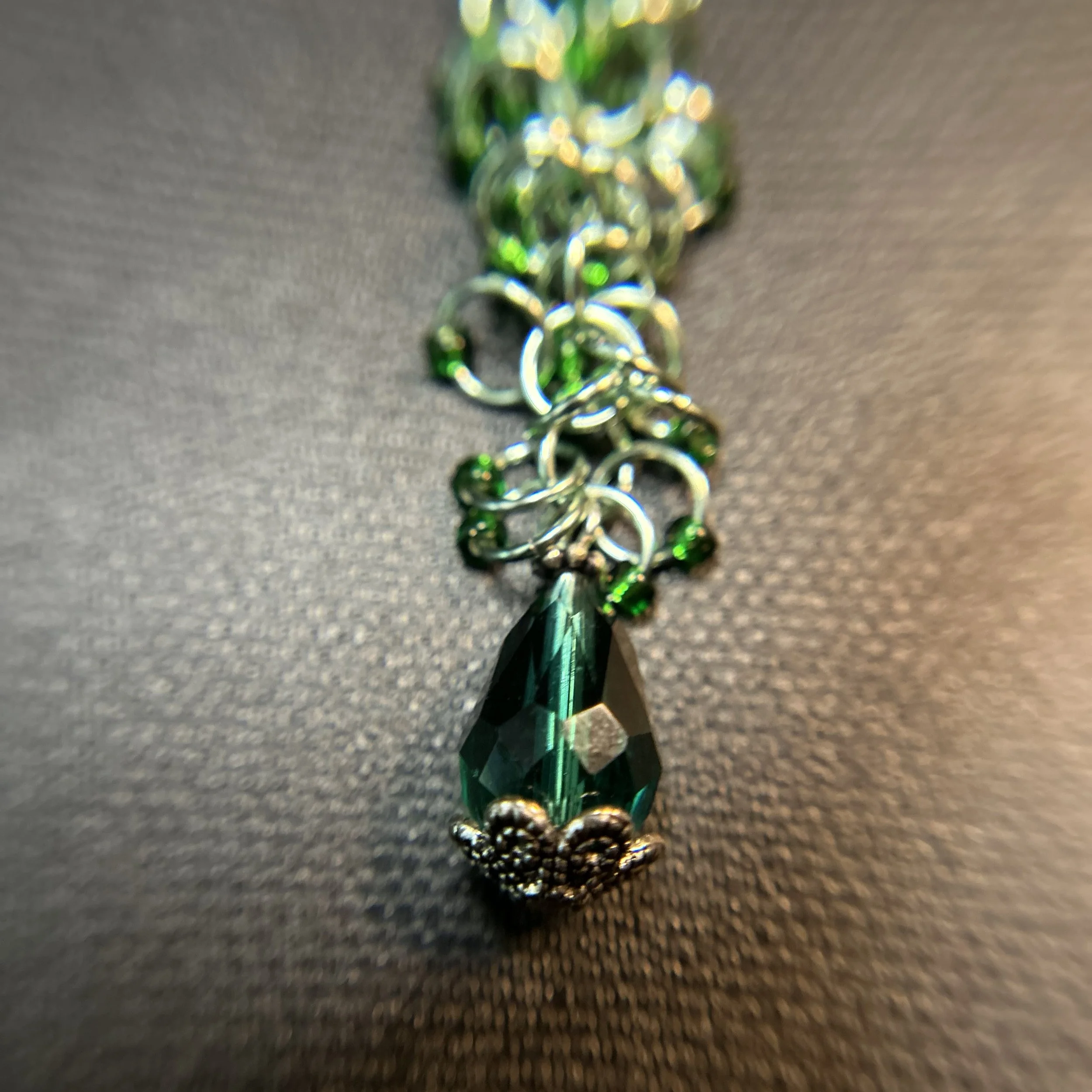 loseup of the faceted green drop on a green chainmaille purse charm.