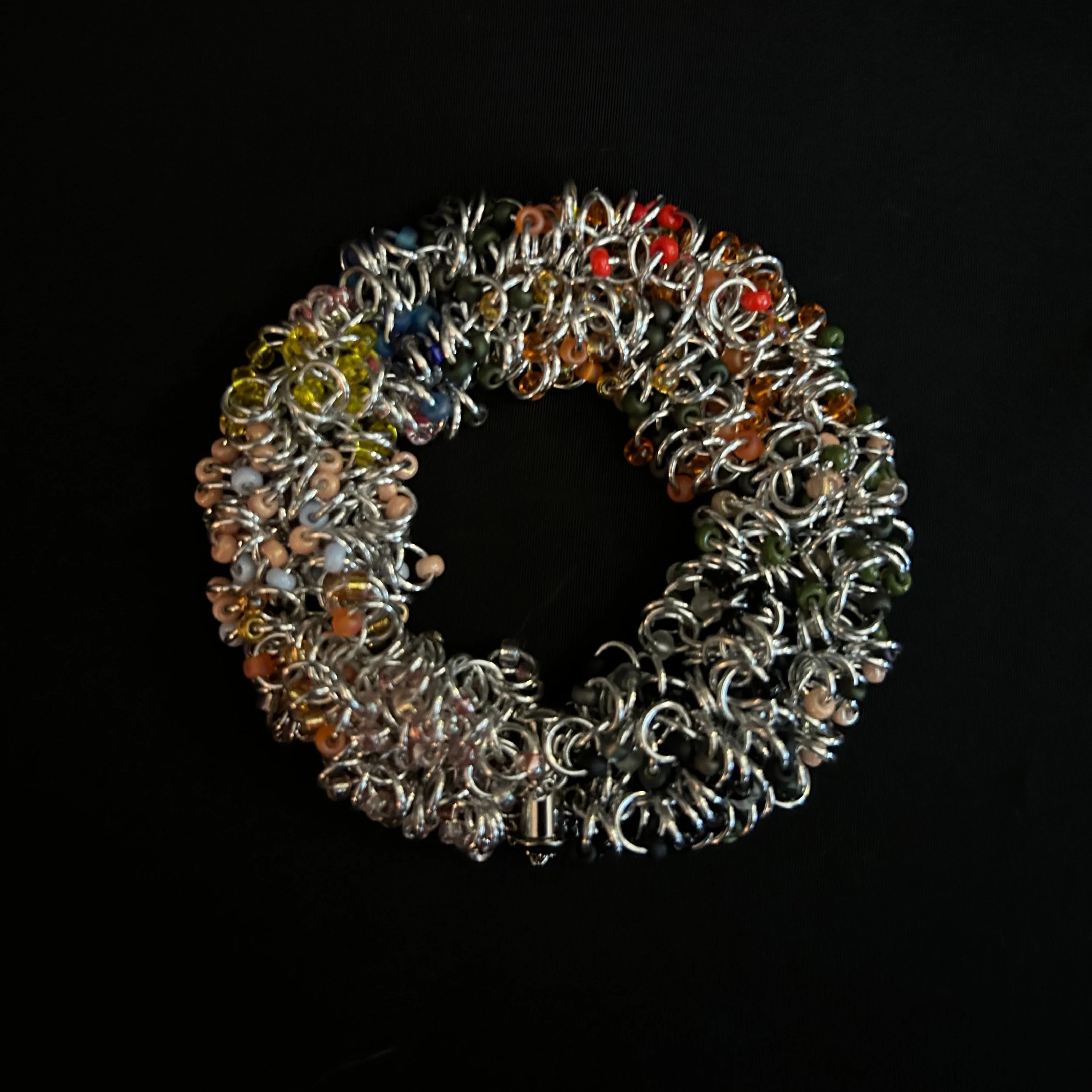 “Blue Ridge Autumn bracelet laid flat in a round shape showing rings and fall‑color beads.”