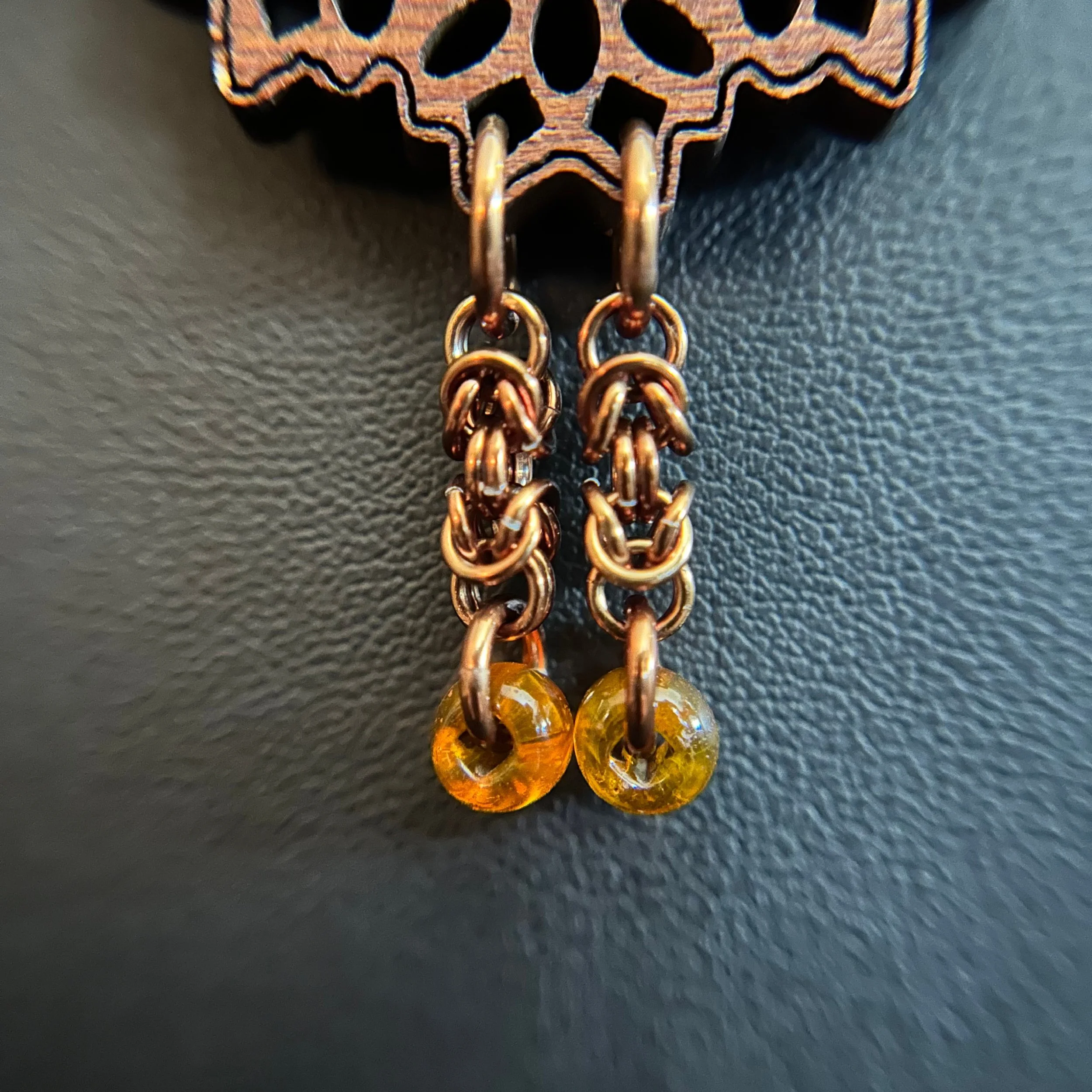 “Close-up of the carved wood focal with bronze chain tassel and amber beads.”
