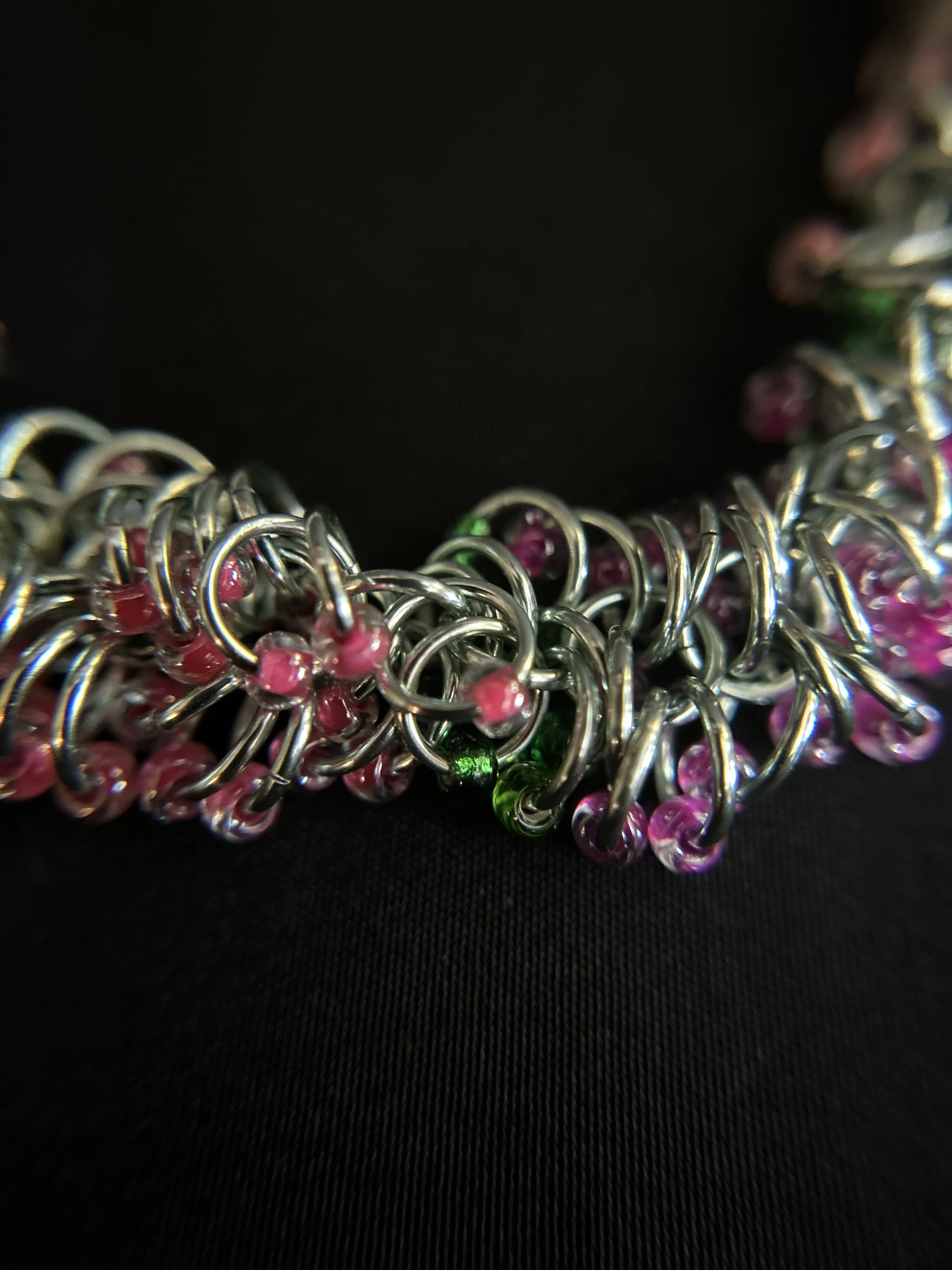 Detailed close‑up of the chainmaille weave with green‑tinged silver rings and pink and green 8/0 Miyuki beads.