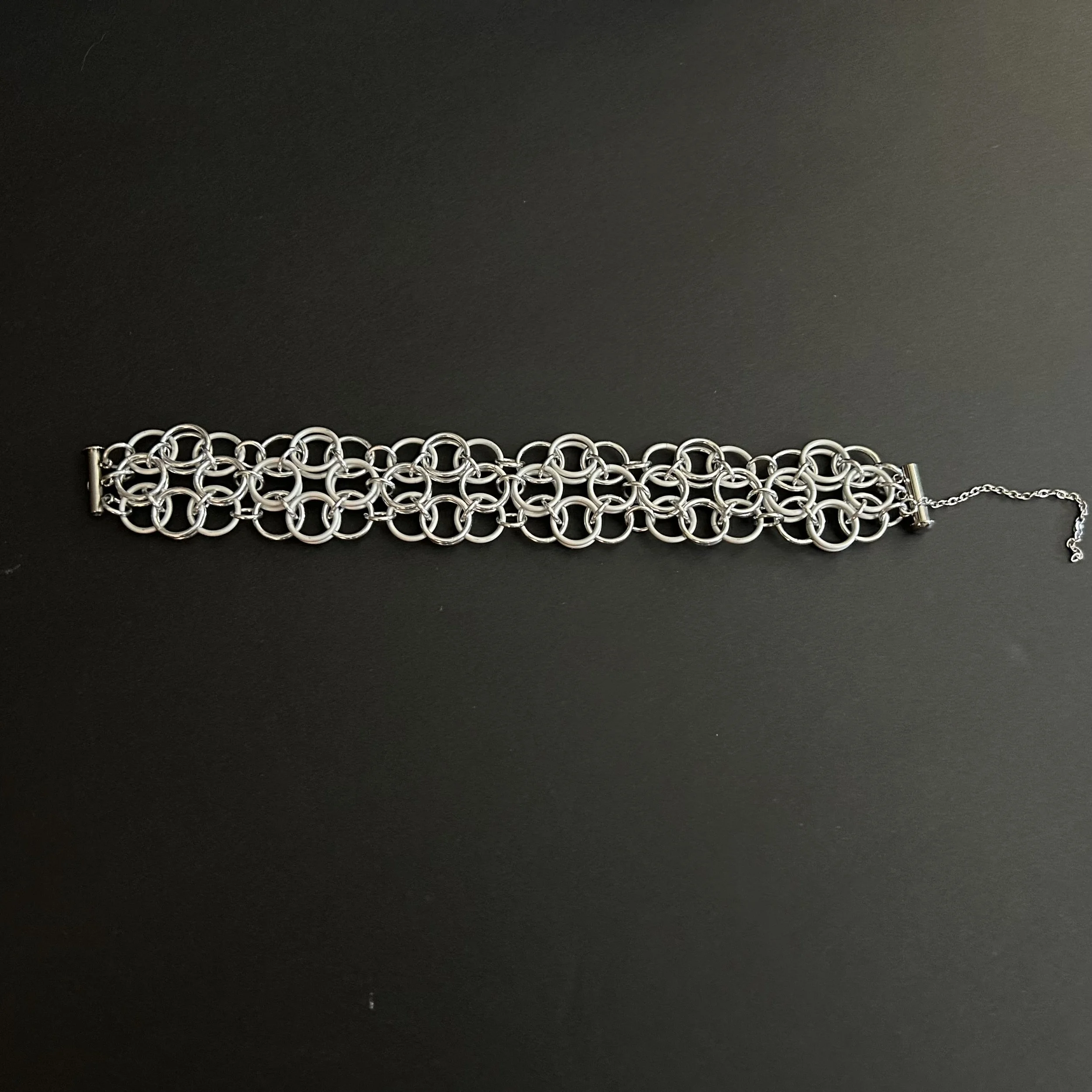 A chainmaille bracelet woven in a helm rosette pattern laid flat on a black background