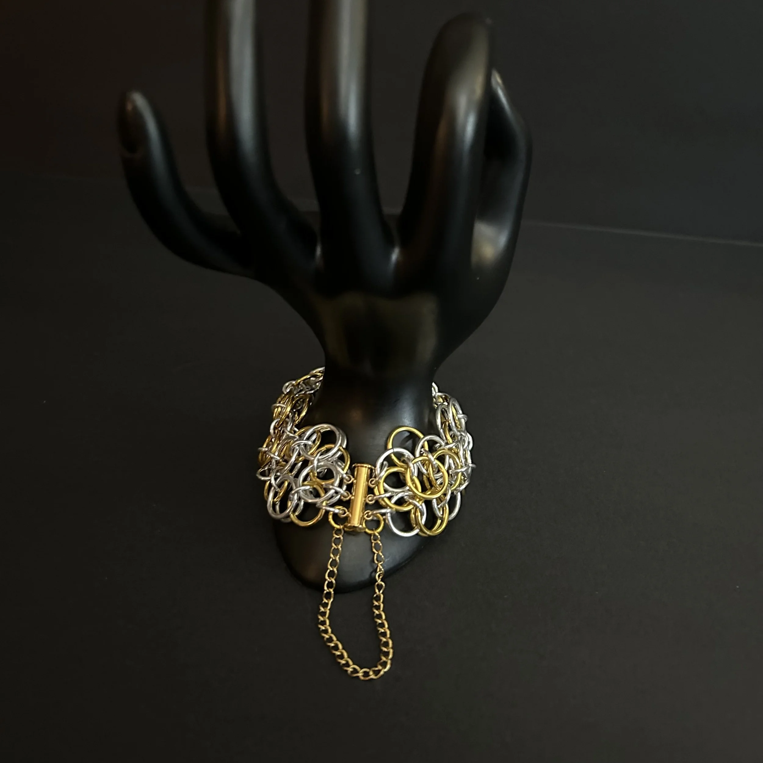 Chainmaille bracelet in sliver- and gold-tone helm rosette weave on hand prop showing clasp detail