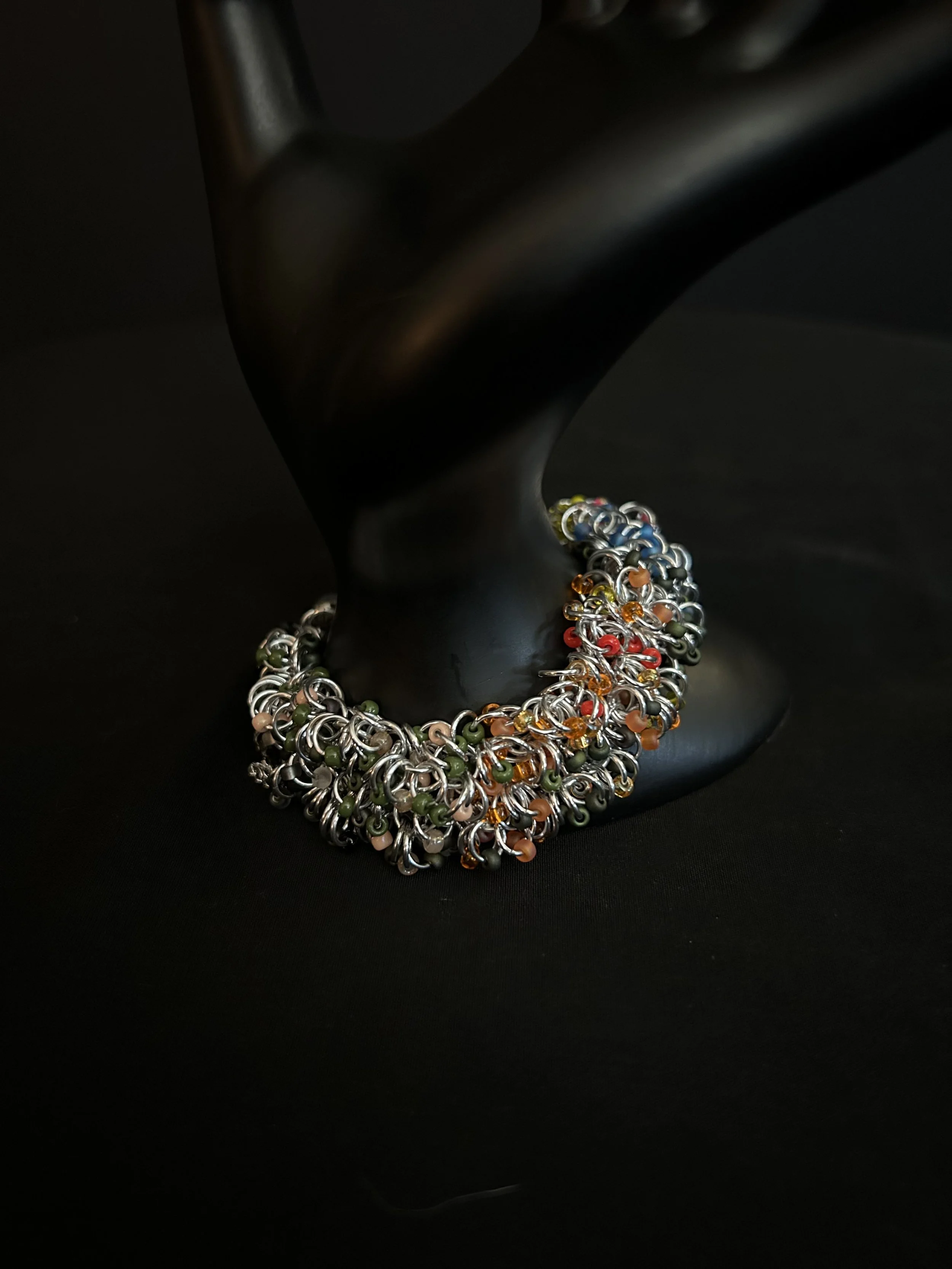 Blue Ridge Autumn bracelet displayed on a black prop, showing the wide silver chainmaille weave with Miyuki beads in warm autumn colors.