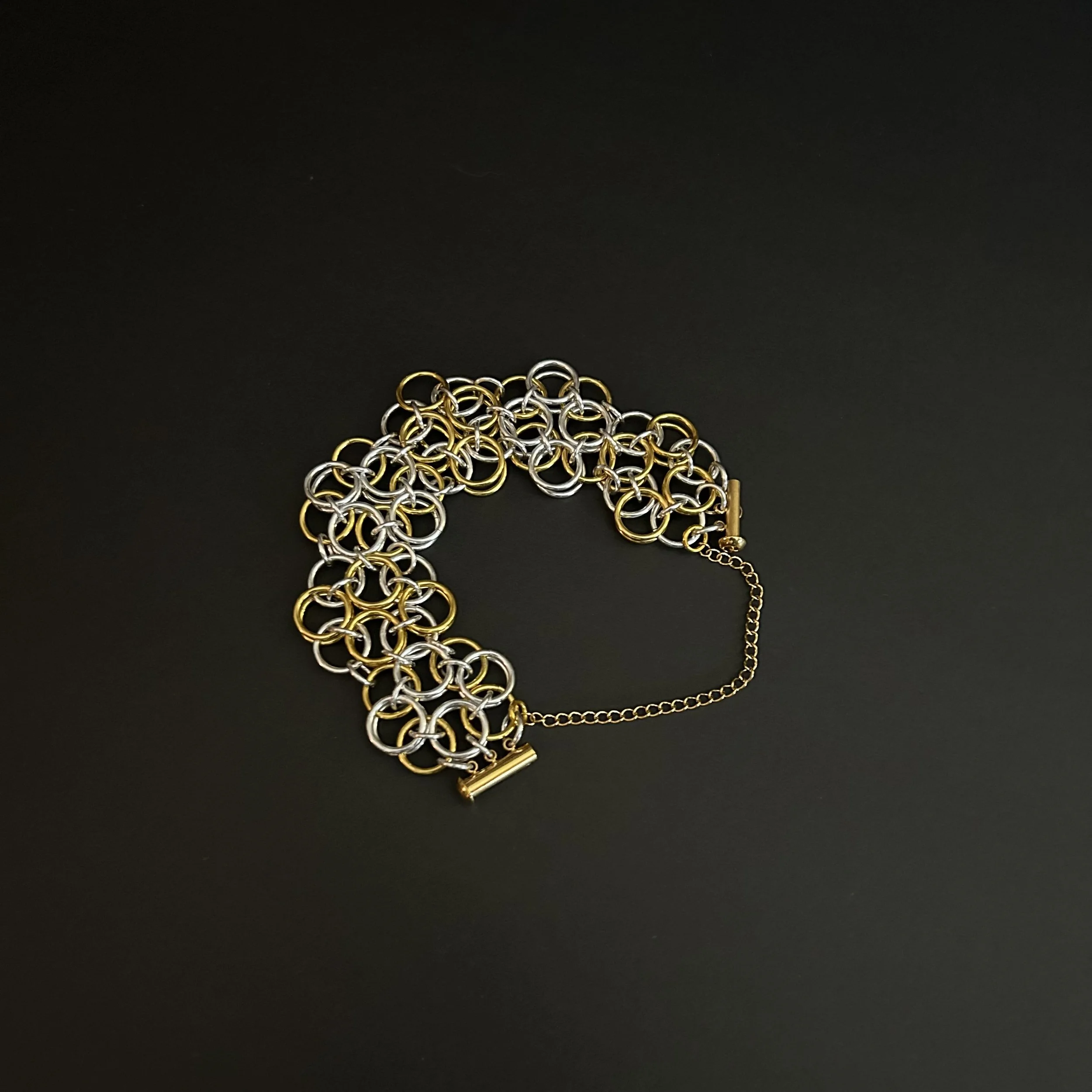 Chainmaille bracelet in sliver- and gold-tone helm rosette weave  shown flat with open clasp