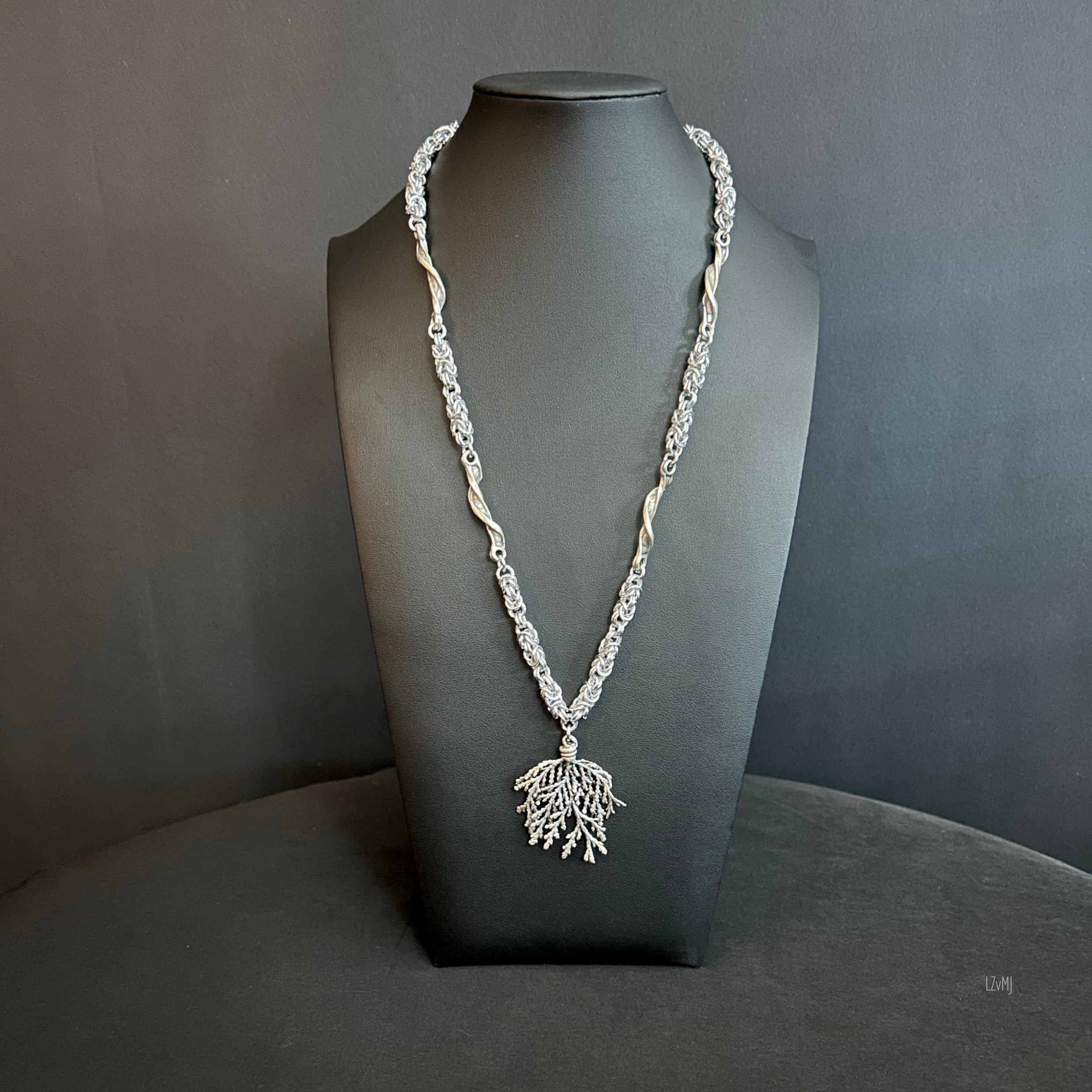 Silver Forest necklace shown on a black bust, featuring alternating twisted chain segments and a detailed branching silver pendant