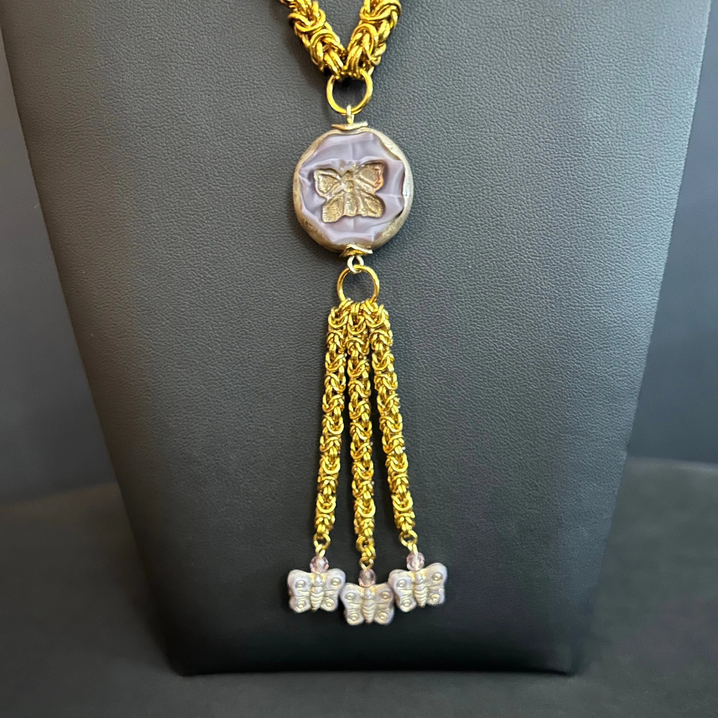 “Close-up of the butterfly focal with three chain tassels ending in butterfly charms.”