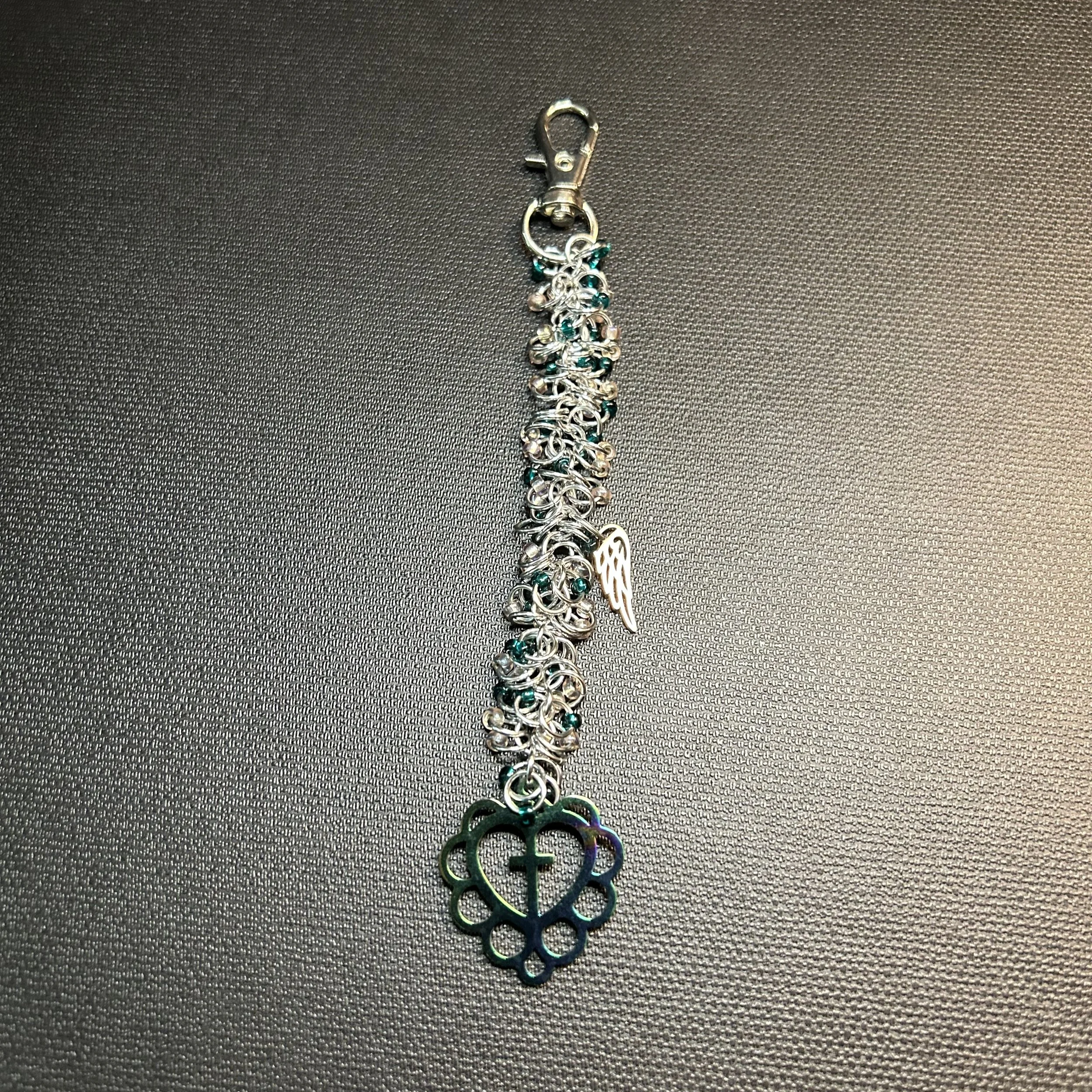 “Close-up of iridescent heart‑and‑cross focal with green and purple color‑shift coating on silver purse charm.”