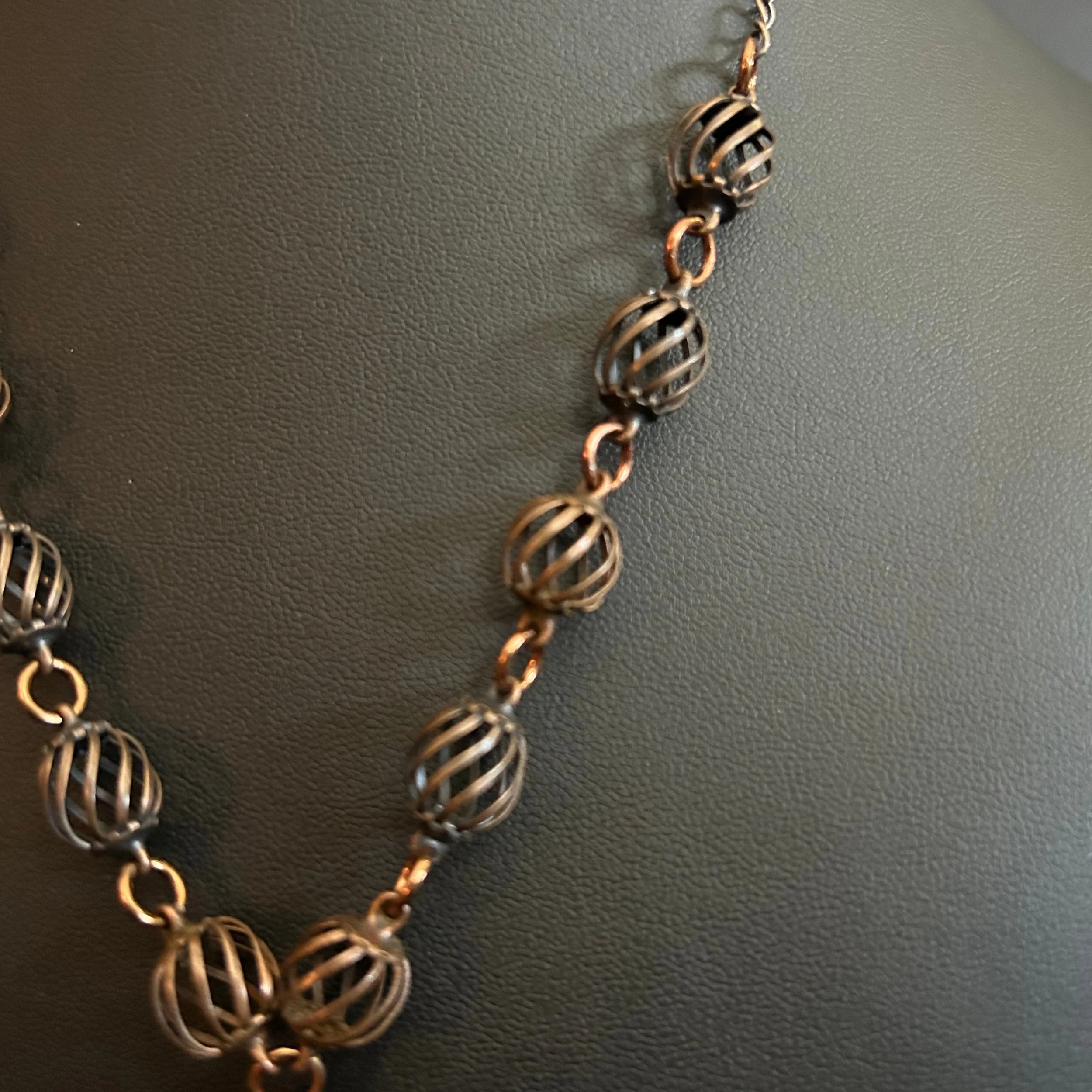 “Detail of the bronze cage‑style beads and connecting chain links.”