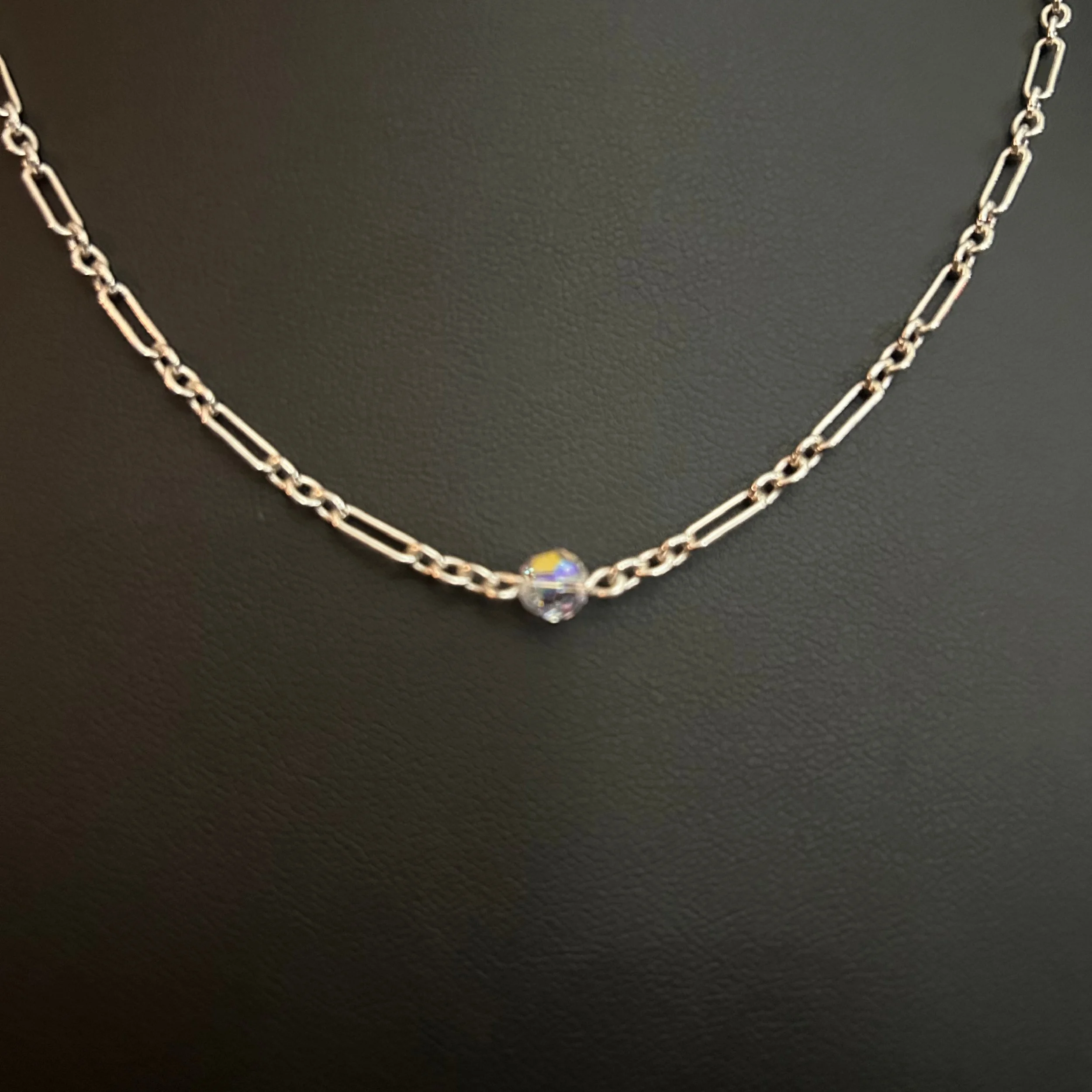 Close-up of the Crystal Whisper Sterling necklace showing the oval silver links and a small iridescent crystal bead