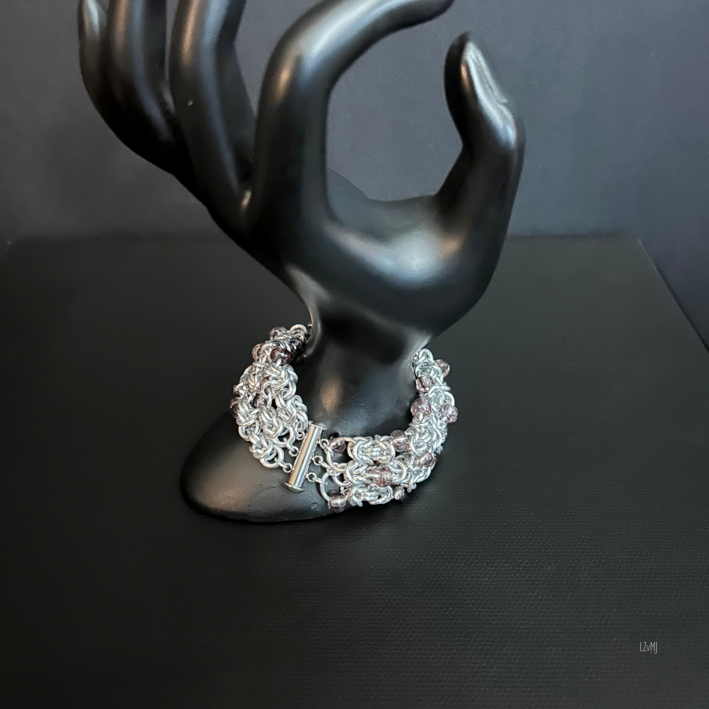 Silverberry Byzantine bracelet on a black mannequin hand, featuring polished aluminum chainmaille, pale purple beads, and a cylindrical clasp.