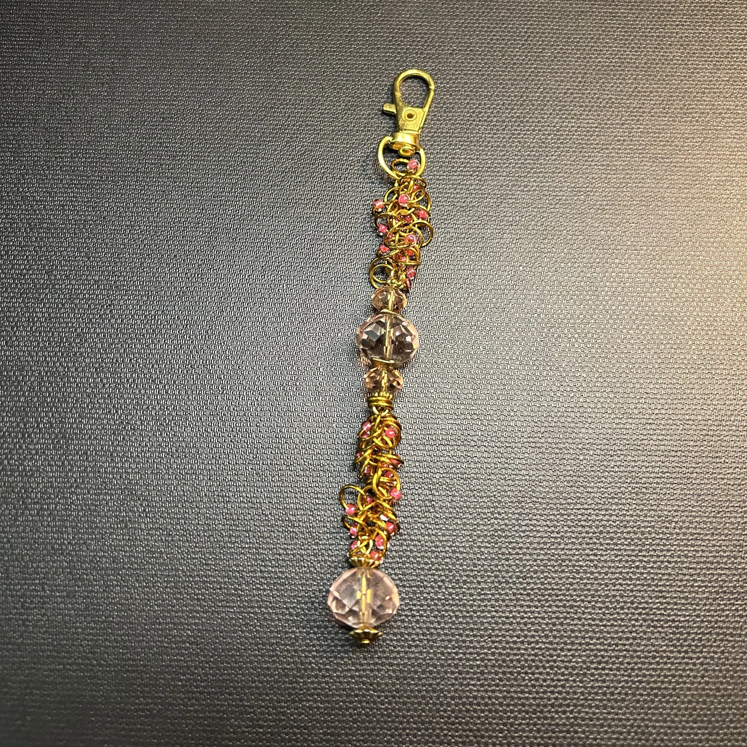 “Gold ring purse charm with pink bead accents and faceted crystal focal, 5.25 inches long with swivel clasp.”