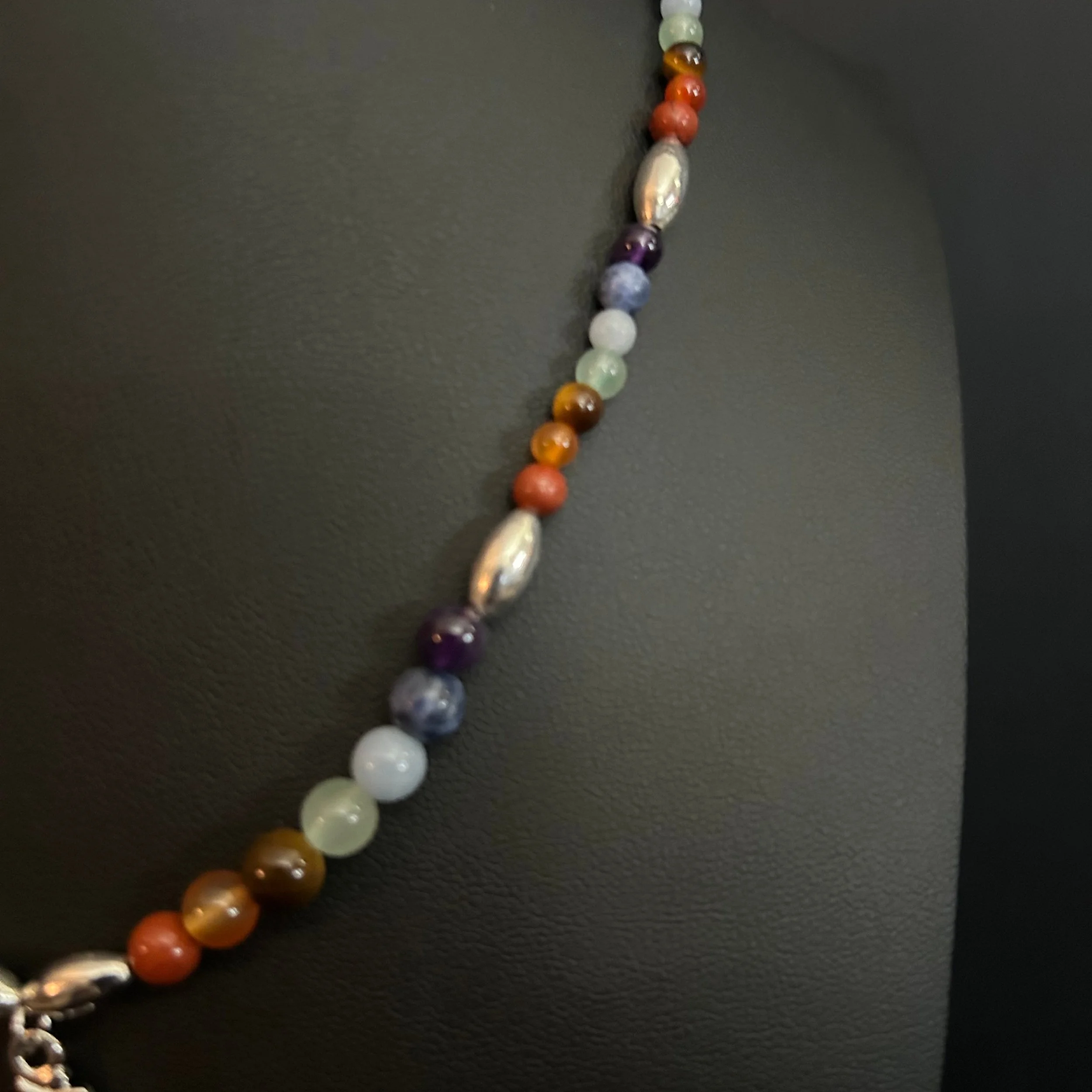 Detail of the Om Balance necklace with polished multicolor gemstone beads and silver accent beads against a dark background