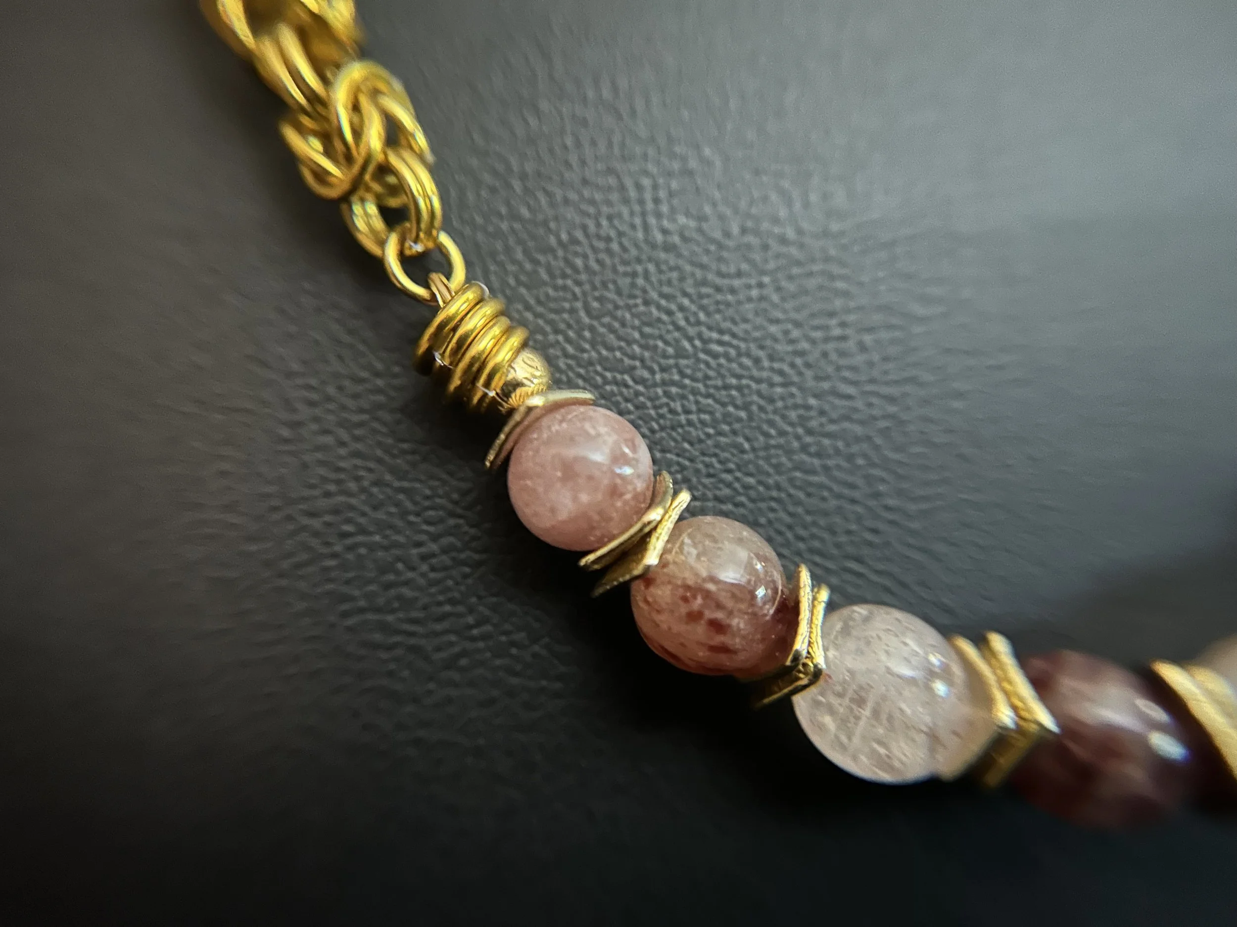 Detail of hand‑woven gold‑tone chainmaille necklace with seven 8mm strawberry quartz beads and gold‑plated spacers,