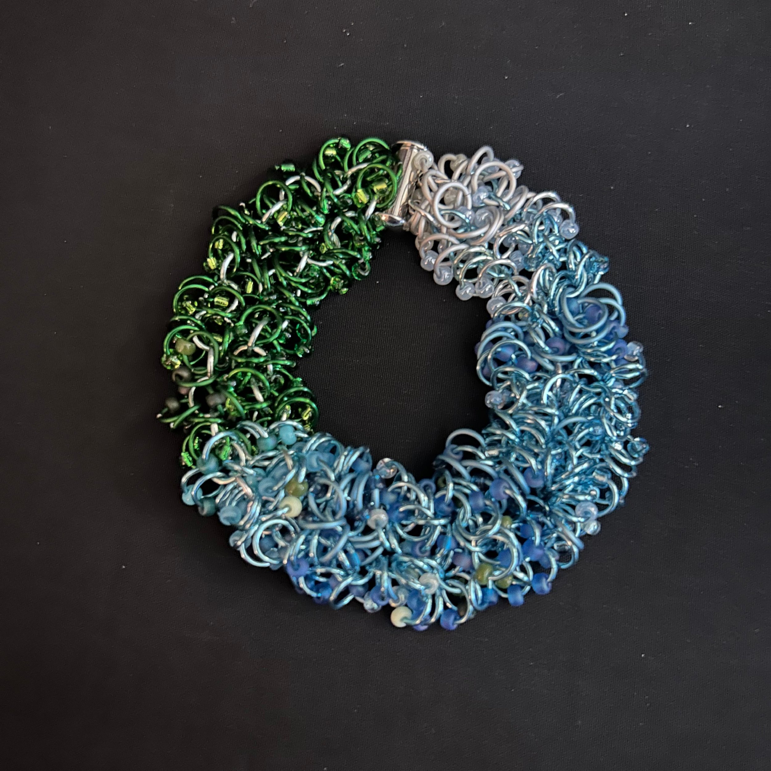 “Blue Ridge Mountain bracelet laid flat in a round shape showing aluminum rings and gradient beads.”