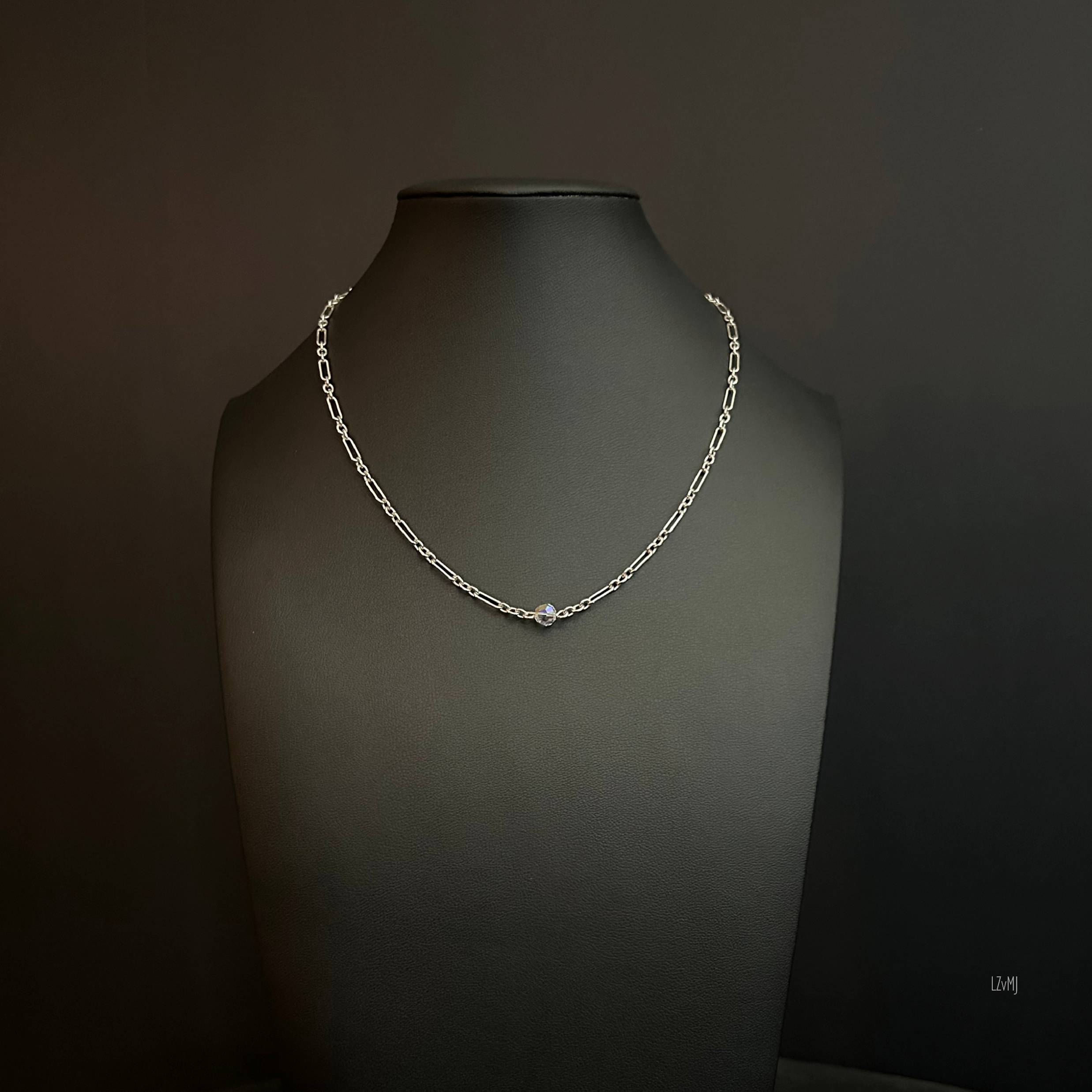 Crystal Whisper Sterling necklace displayed on a black stand, with elongated silver links and a single luminous crystal bead at the center.