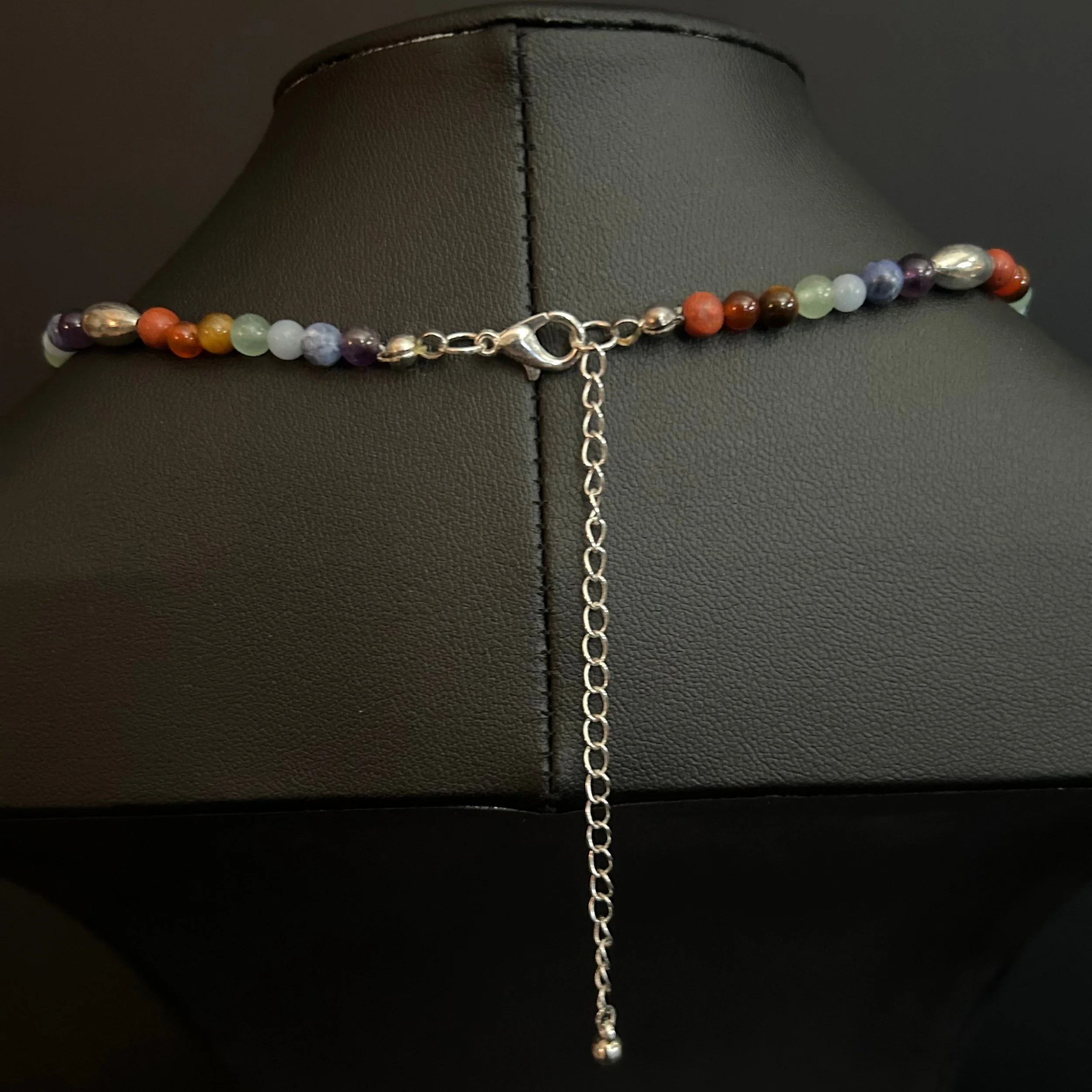 Close-up of the Om Balance necklace showing the silver lobster clasp, extension chain, and multicolor gemstone beads