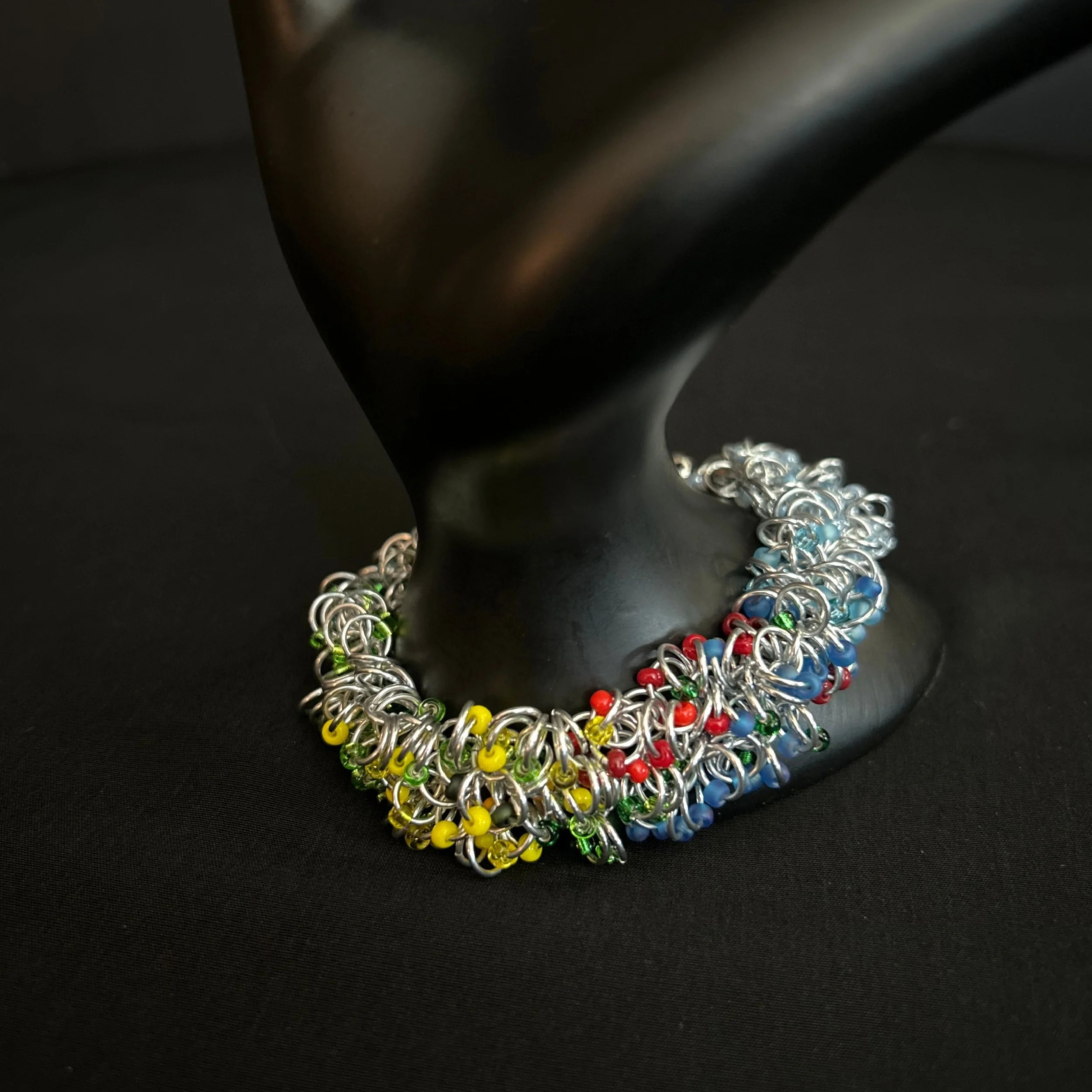 “Aluminum chainmaille bracelet with summer‑tone Miyuki beads draped over a display prop.”