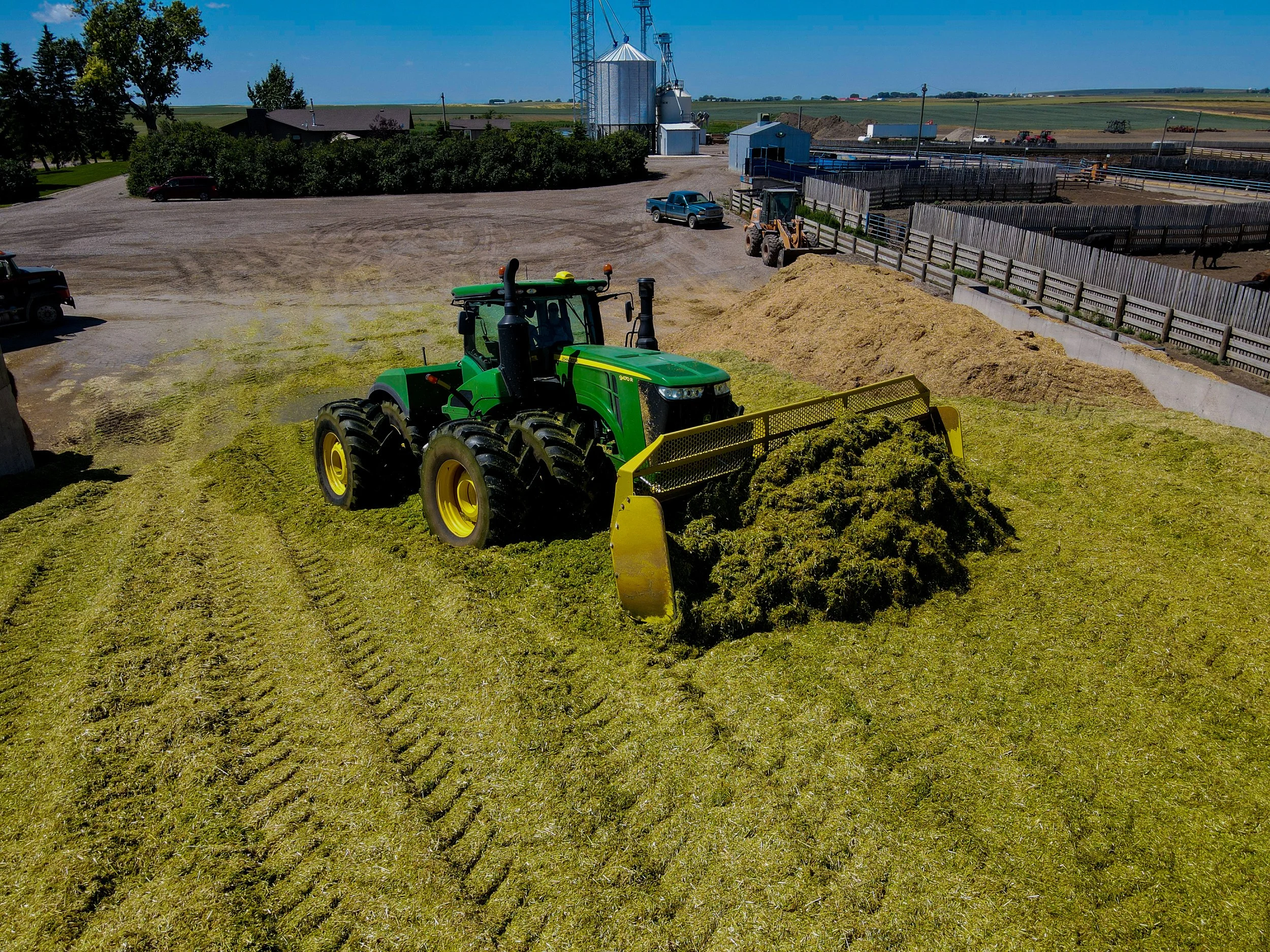 Green tractor spreading freshly cut forage and pushing it onto a pile to allow it to ferment.